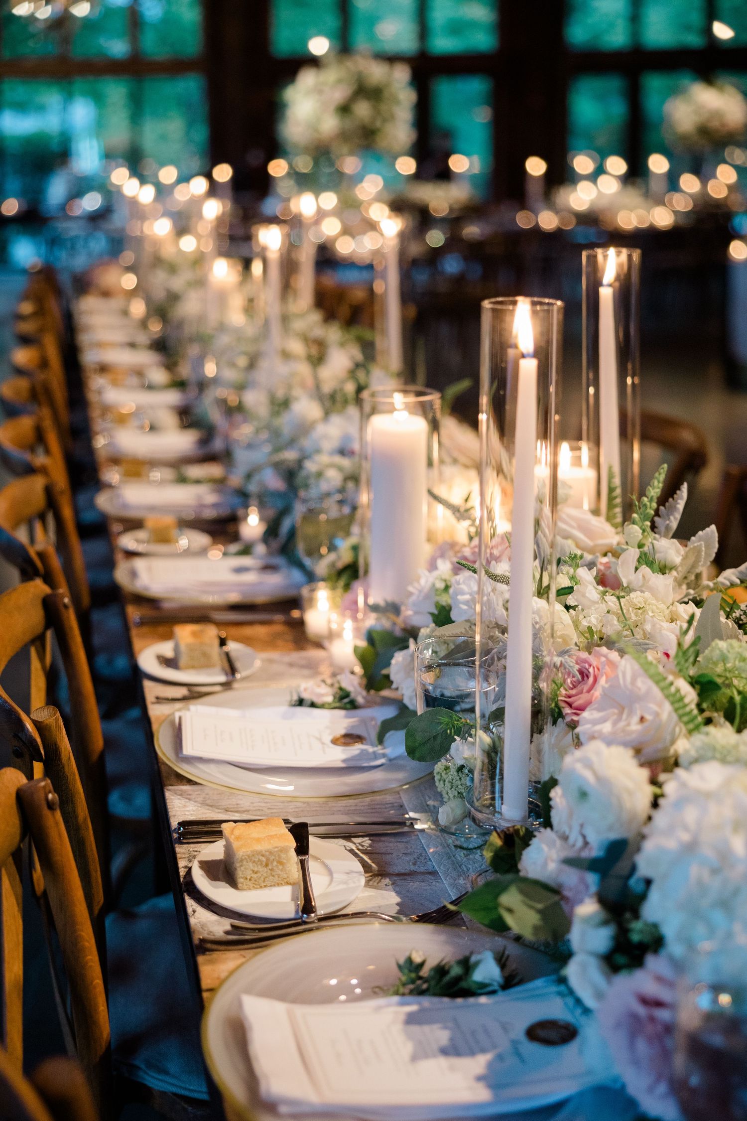 Luxurious wedding table setting with white floral arrangements and tall candles in glass holders.