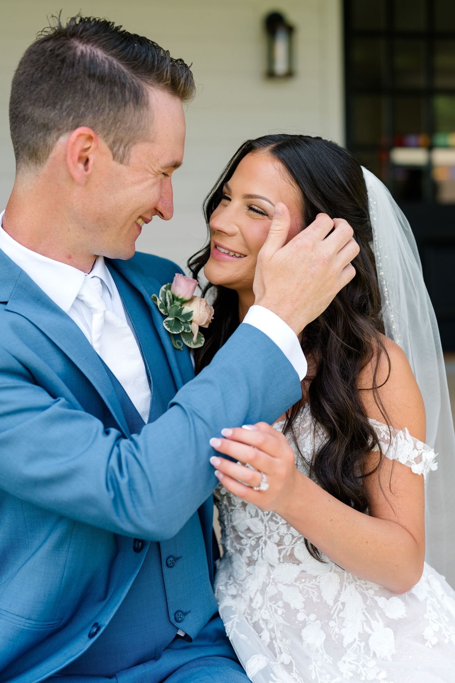 Intimate moment between newlyweds in blue suit and white lace dress.