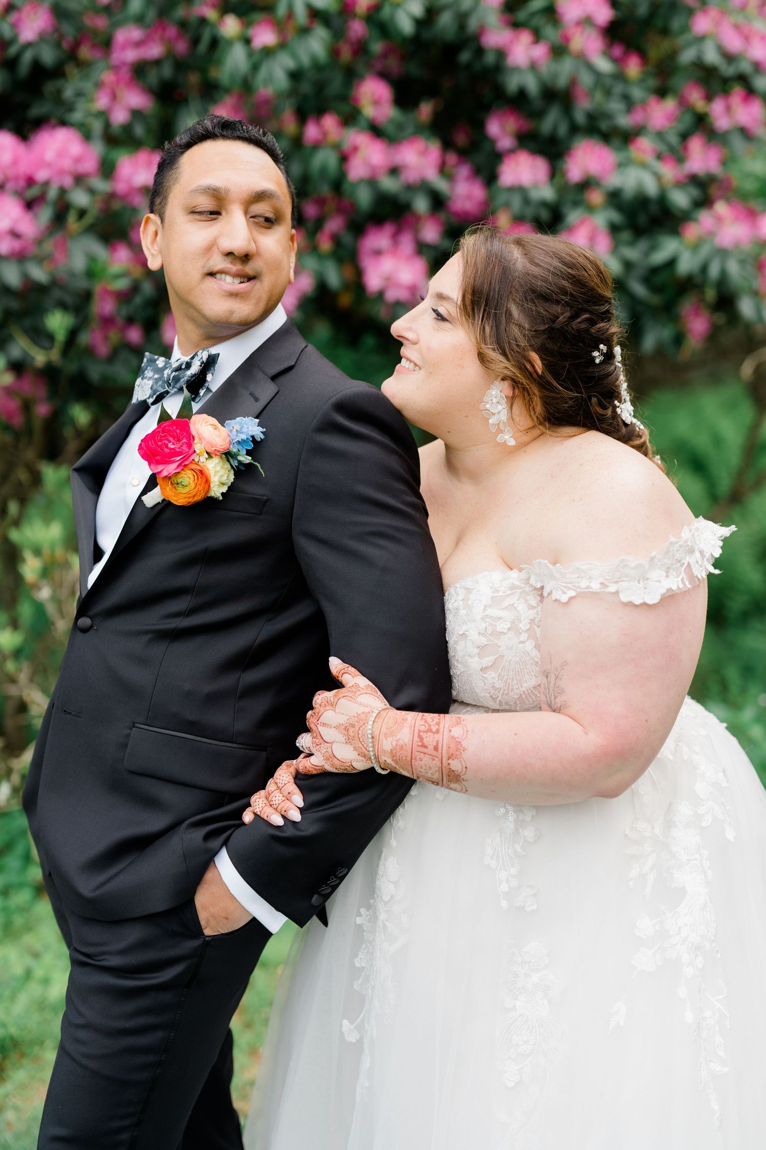 A couple in wedding attire share romantic moments together in front of pink flowering bushes.