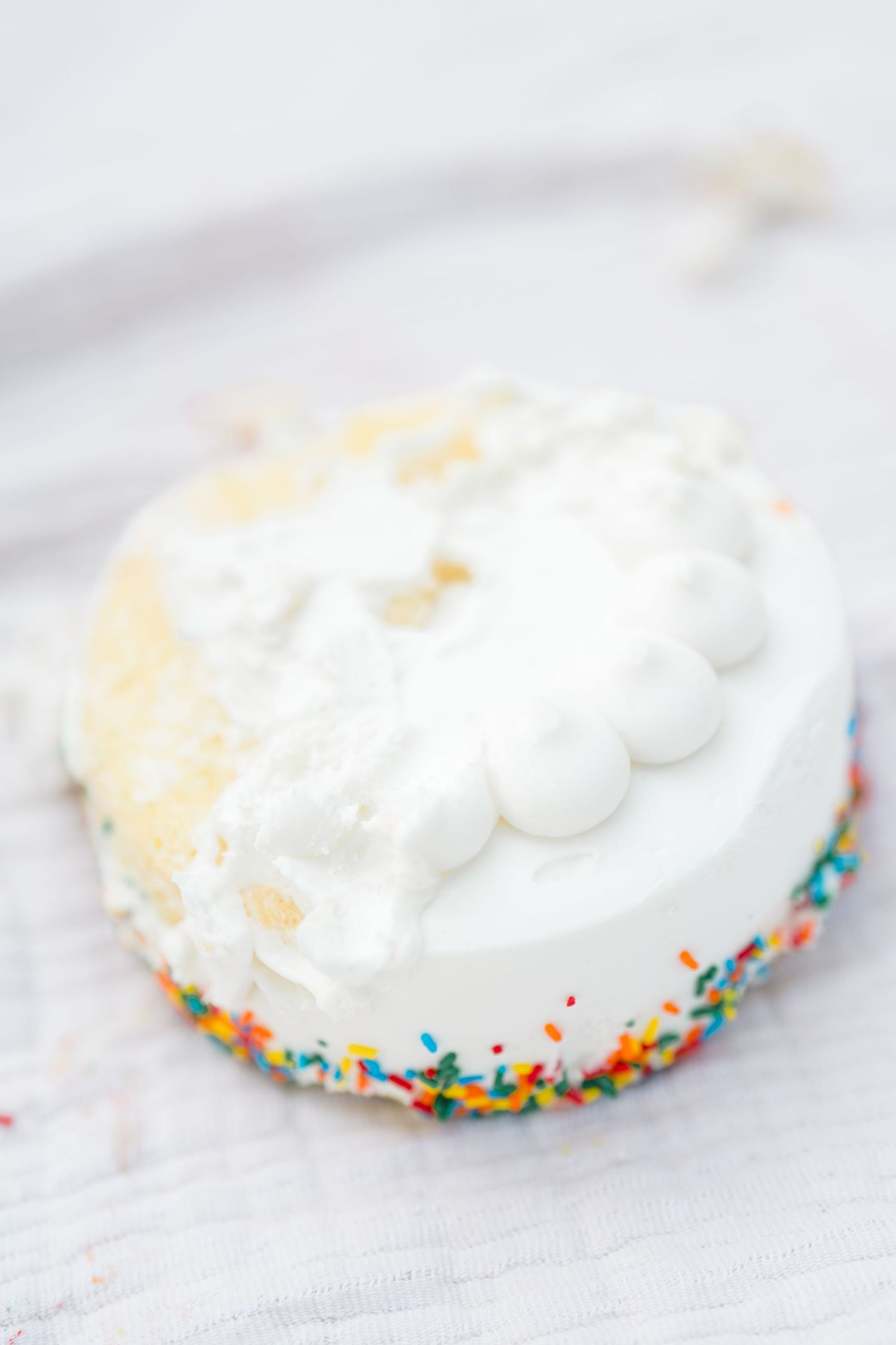 Small white smash cake with colorful sprinkles and white frosting on a white surface.