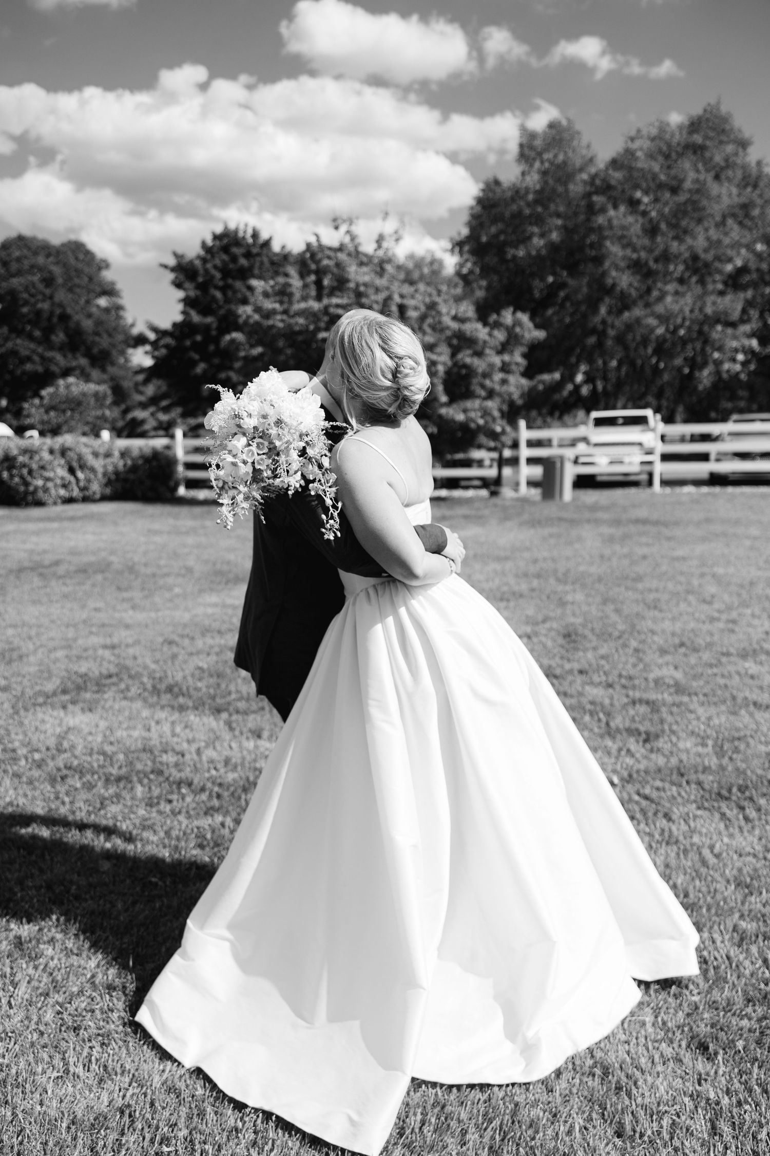 Black and white photo of a bride and groom embracing on a green lawn after their ceremony.