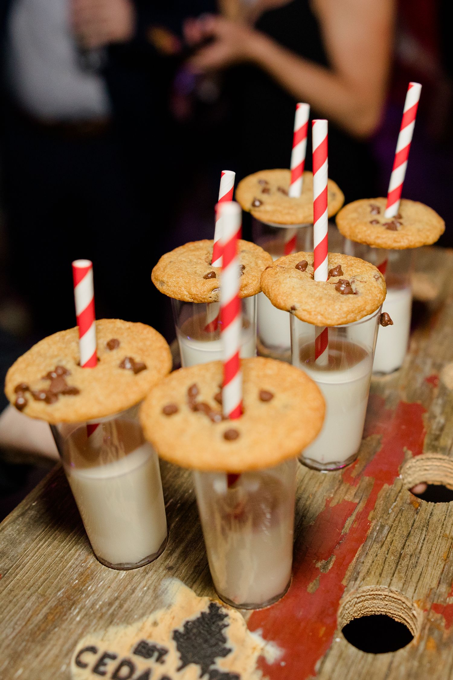 Chocolate chip cookies served on milk shooters with striped straws at a wedding reception.