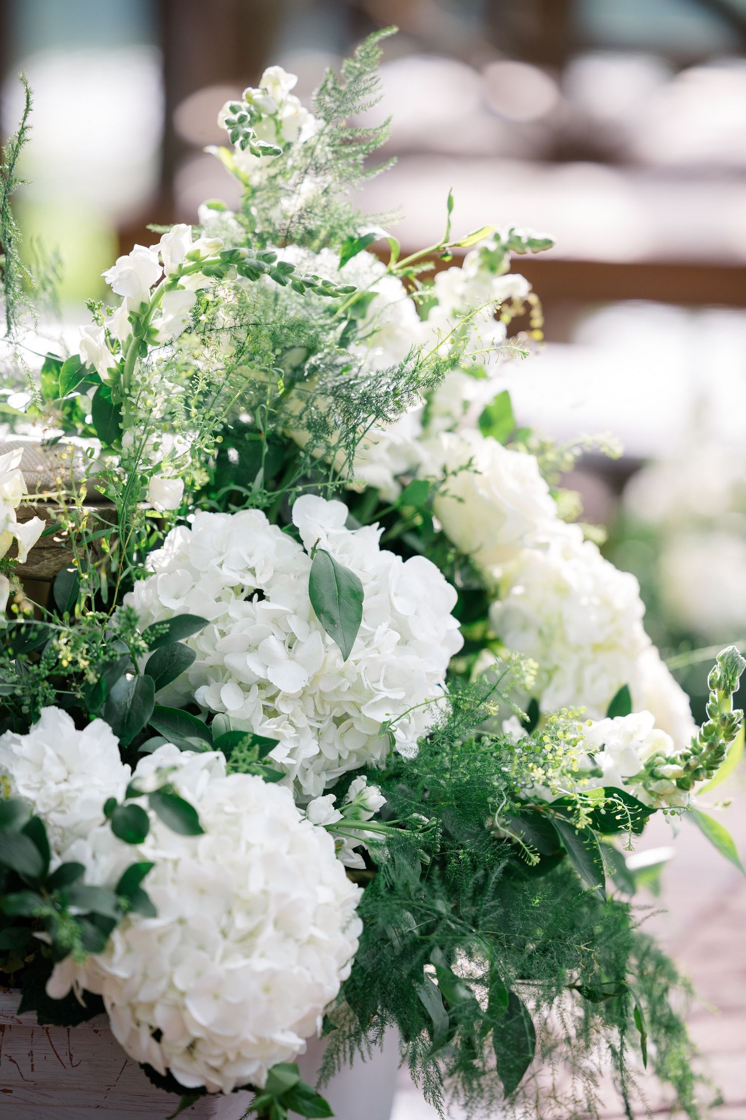Elegant white floral arrangement with hydrangeas and delicate greenery for a wedding centerpiece.