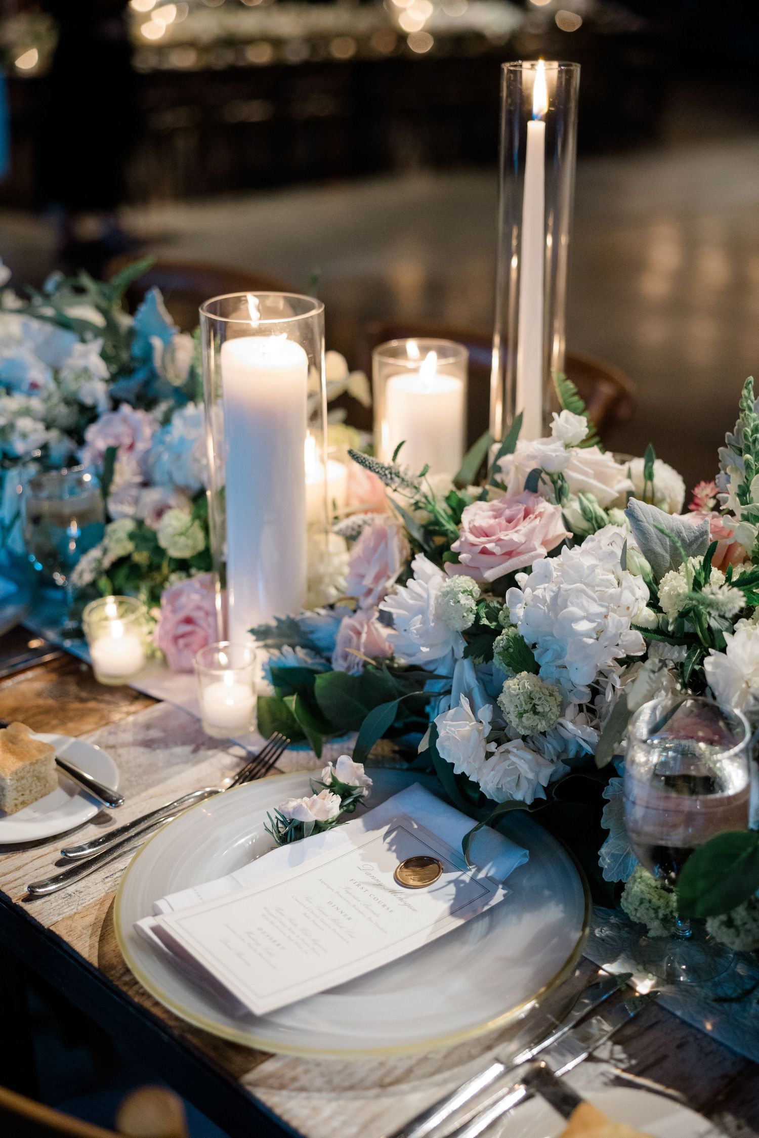 Elegant wedding table setting with white candles, blue and pink floral arrangements, and formal place settings.