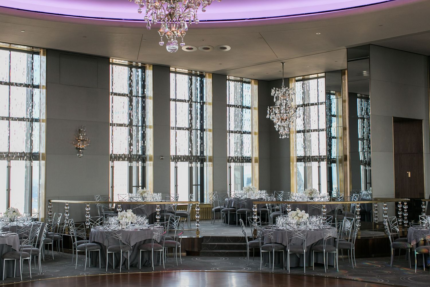 Elegant reception hall with crystal chandeliers, floor-to-ceiling windows, and silver table settings.