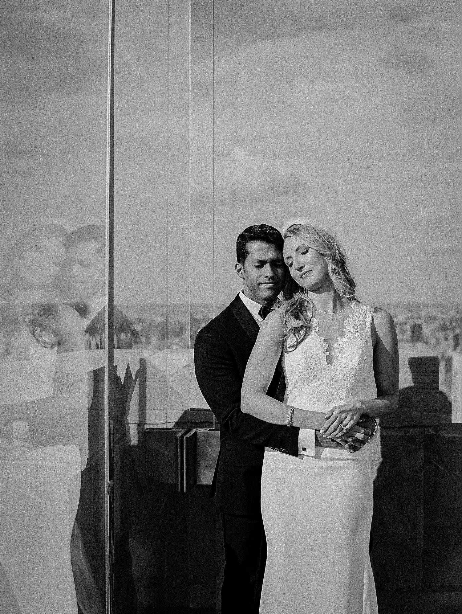 A romantic black and white portrait of a couple in formal attire against a city backdrop.