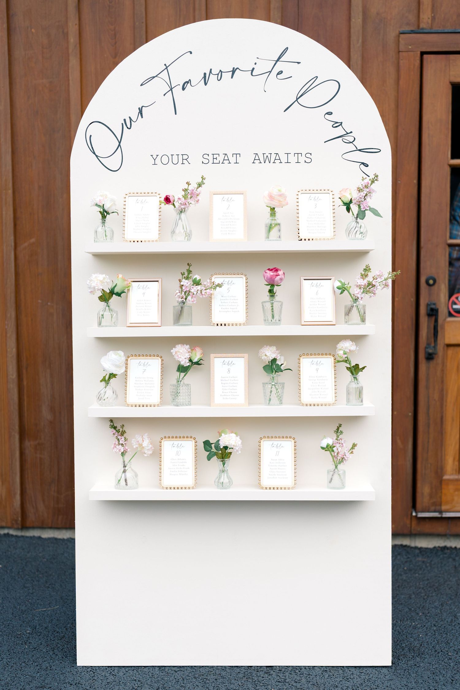 White arched seating chart display with small vases of flowers and table assignment cards.