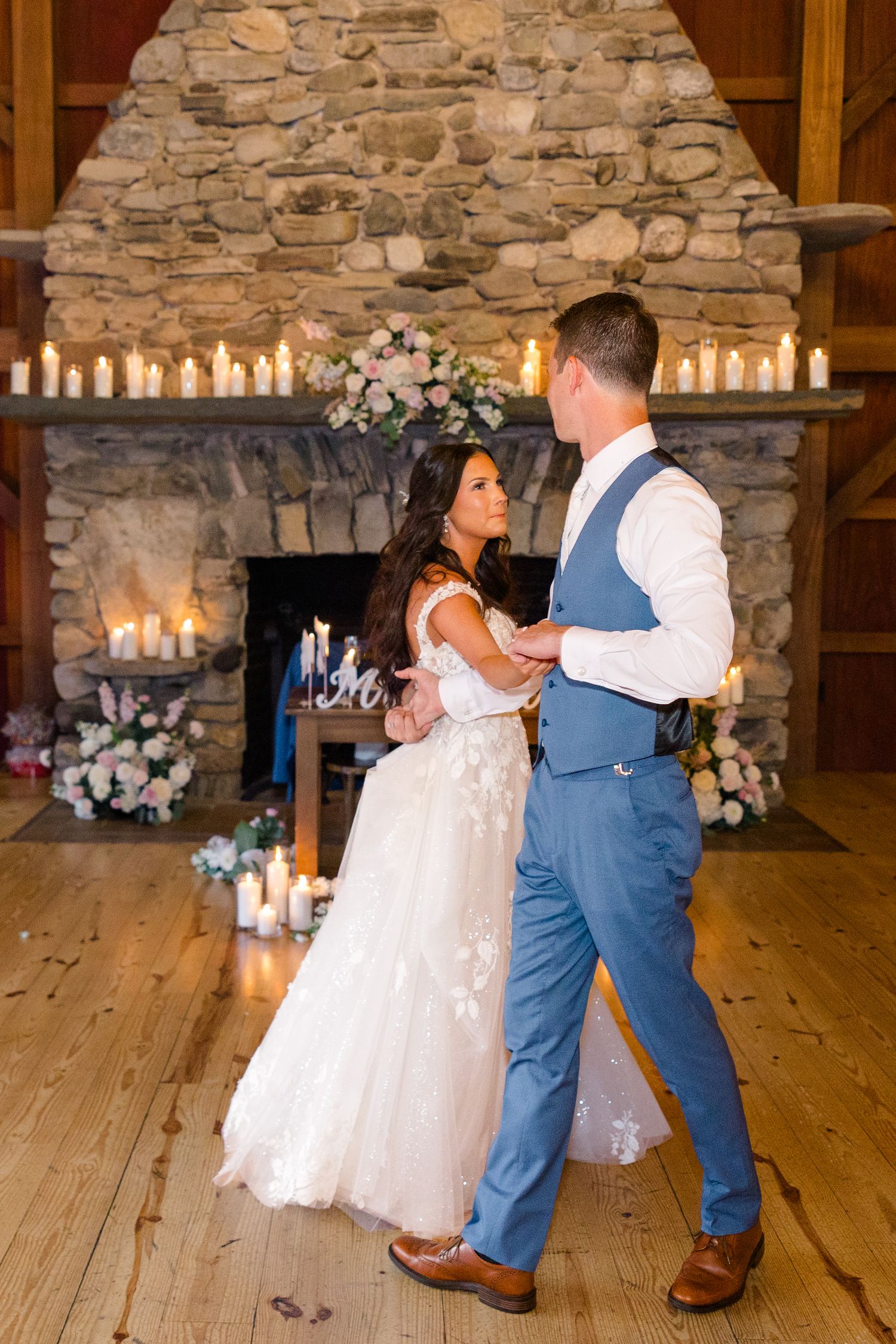 First dance moment in rustic barn venue with stone fireplace and romantic candlelight.