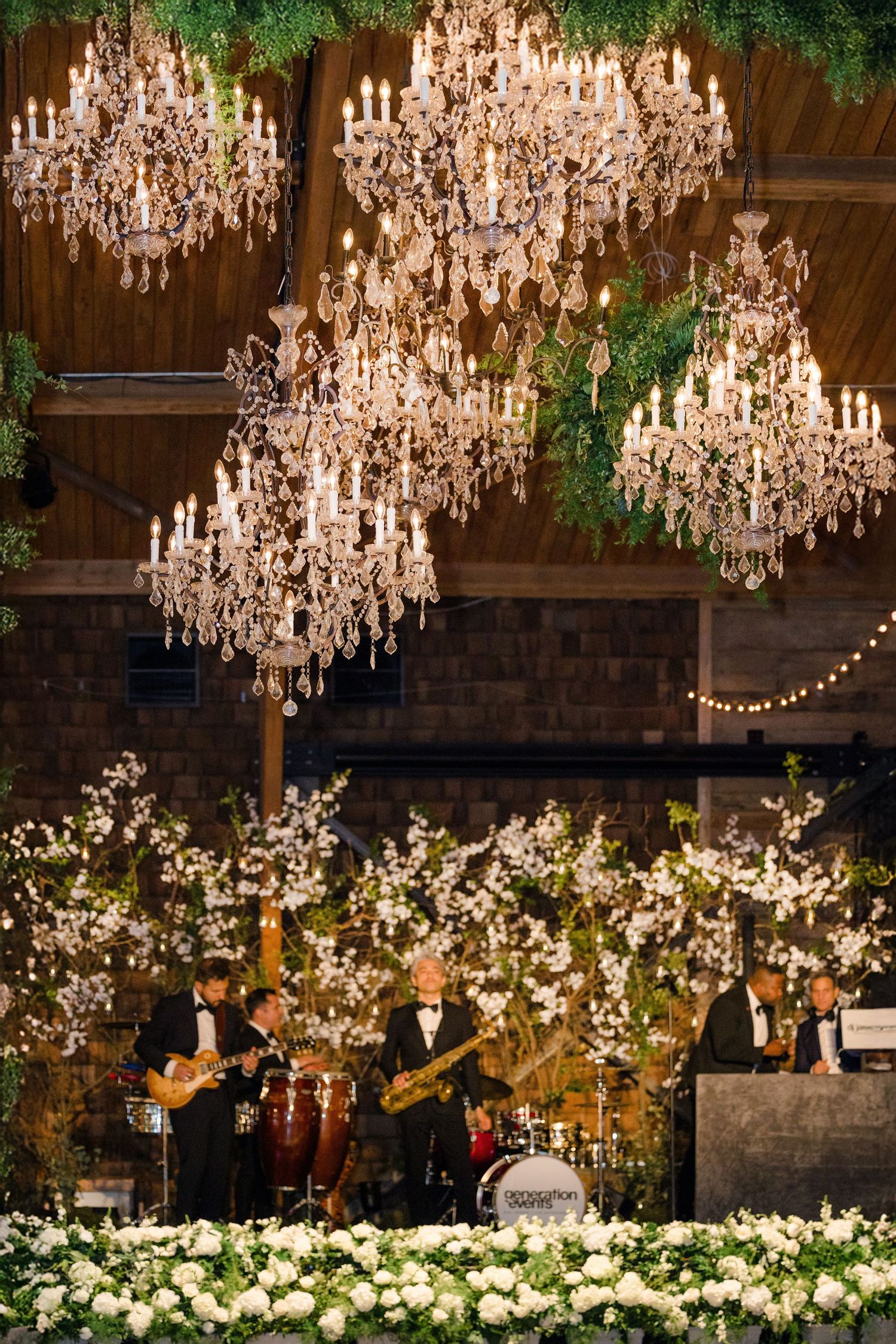 Elegant wedding reception venue with crystal chandeliers hanging over white floral arrangements and string lights.