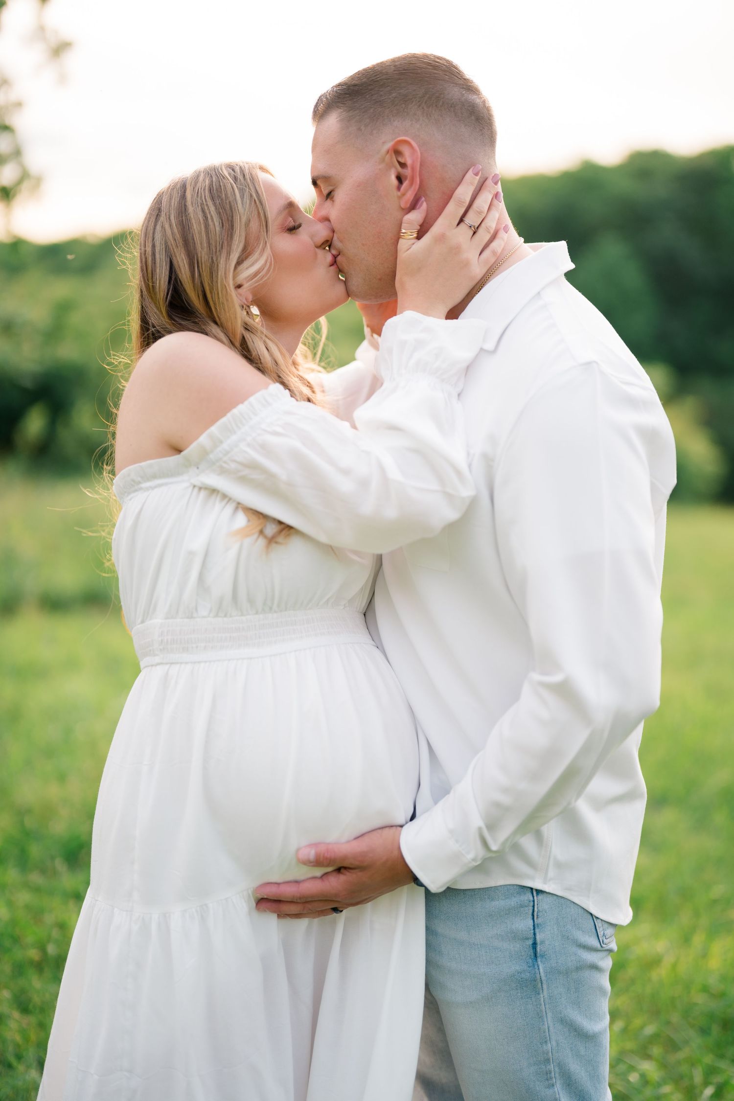 Romantic maternity photo capturing couple's kiss in a sunny garden setting.
