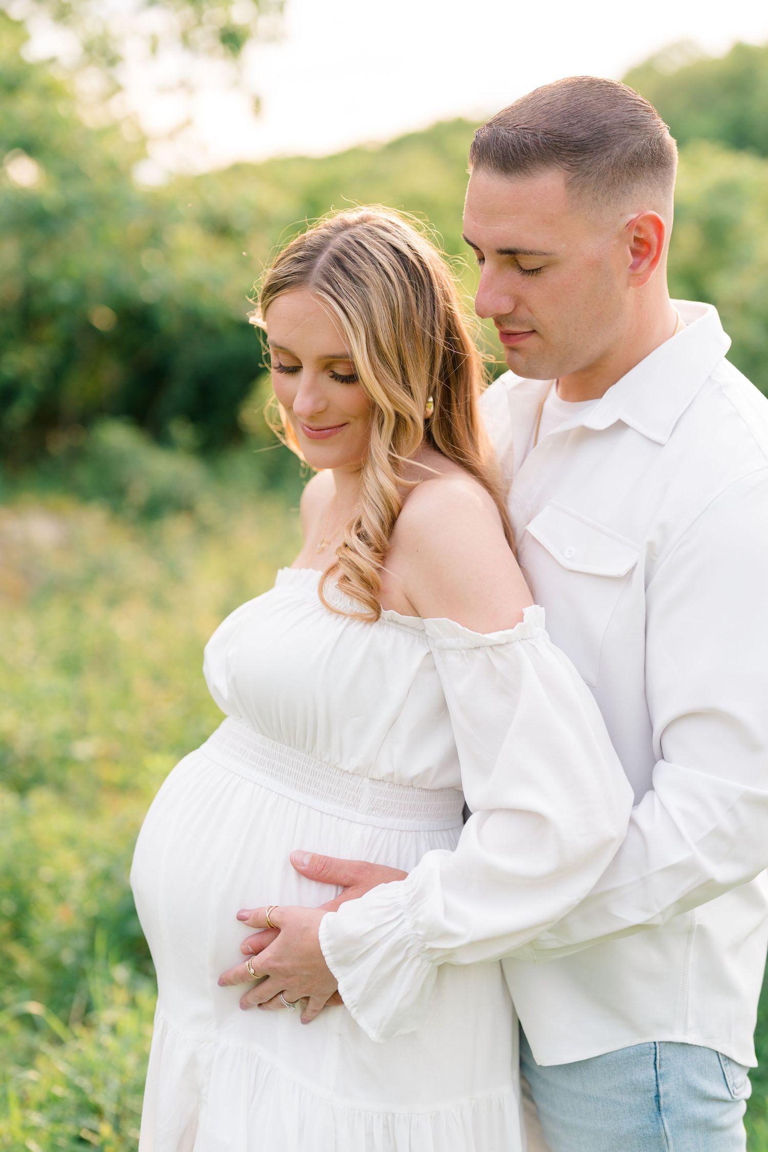 Romantic outdoor maternity photos showing tender moments between expecting couple in white outfits.