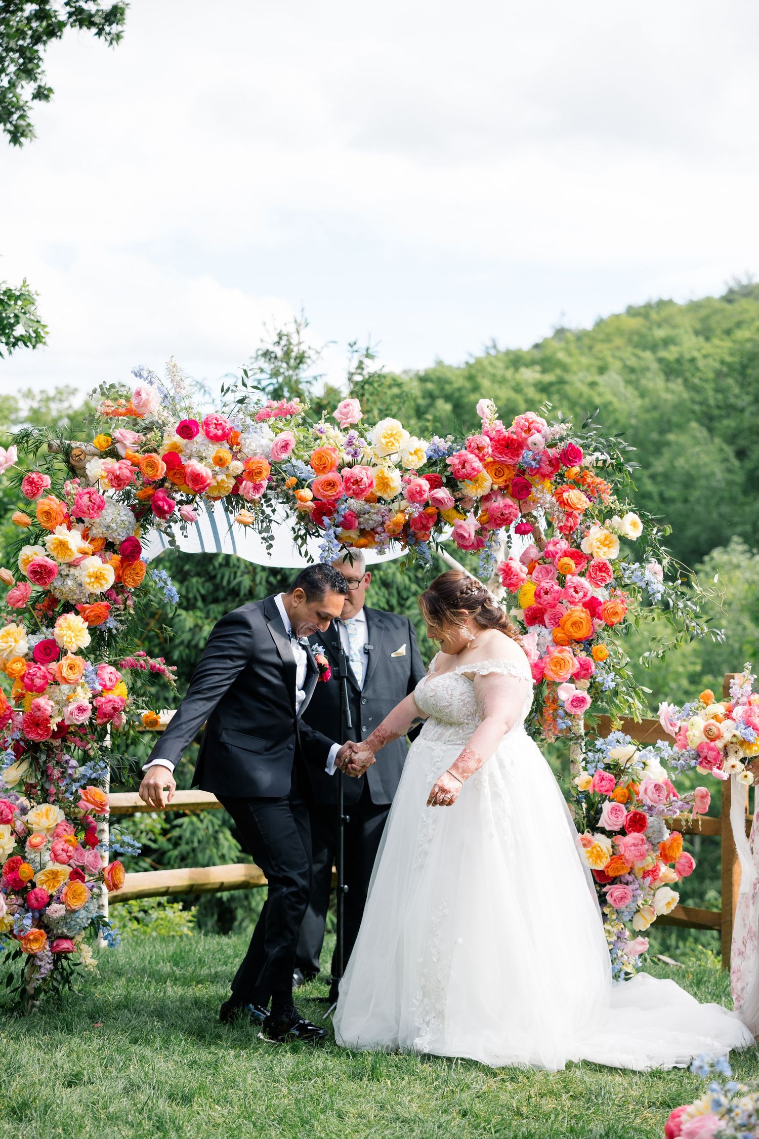 Stunning floral wedding arch with vibrant pink and coral flowers for outdoor ceremony in hillside setting.