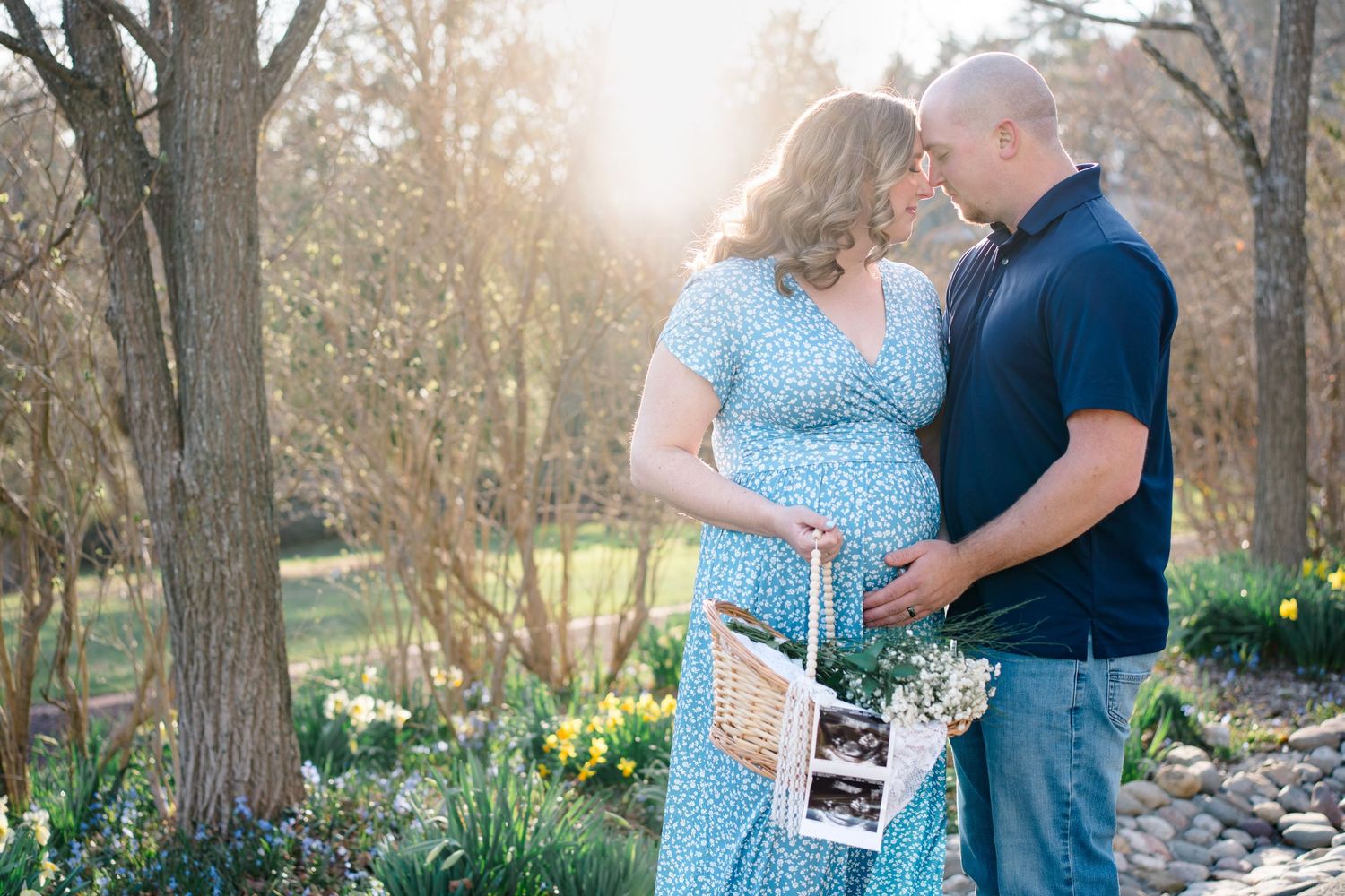 A romantic maternity photo session in a wooded area with blooming spring daffodils on a sunny afternoon.