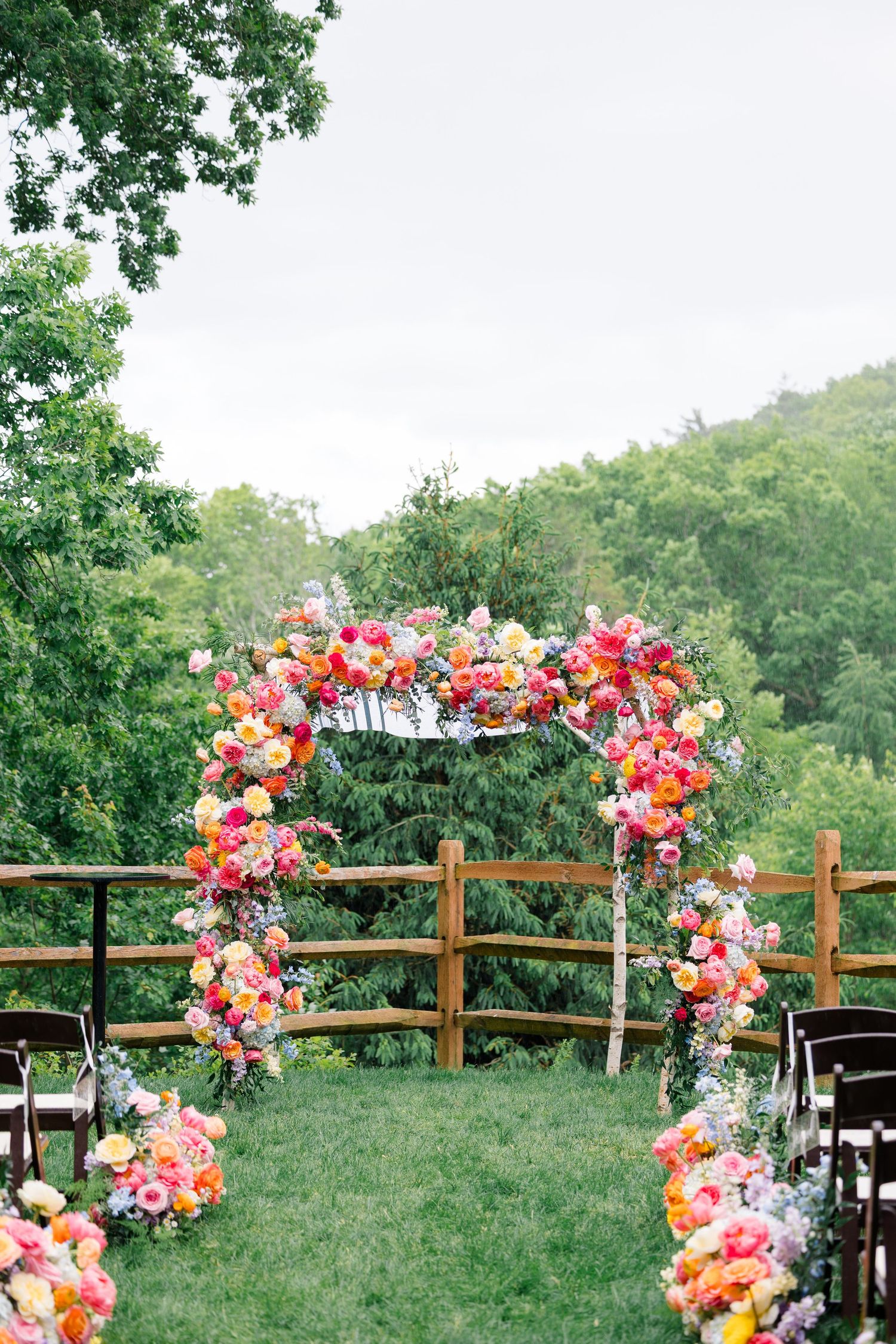 Floral wedding arch with pink and coral blooms overlooking a scenic mountain view with chairs setup for ceremony.