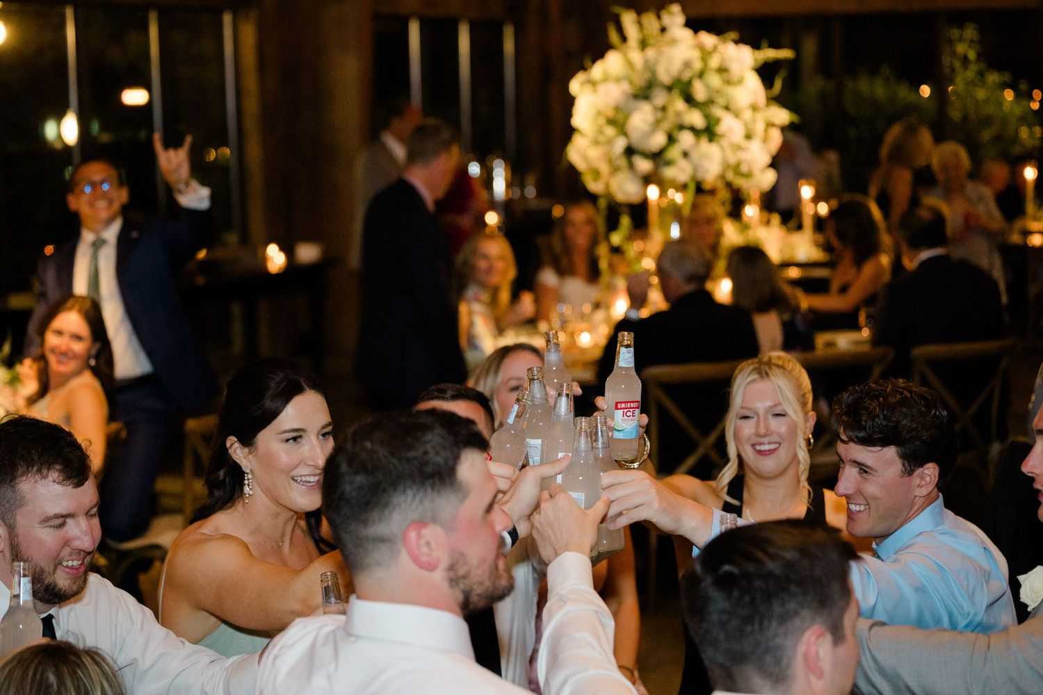 Wedding reception guests raising glasses in a toast during dinner celebration.