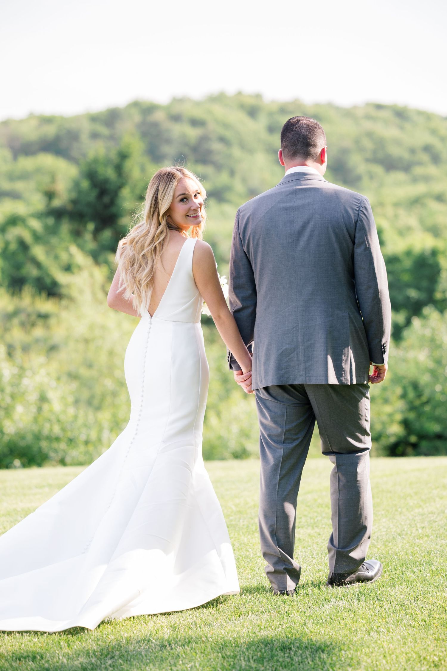 A couple poses together on a grassy hilltop during their outdoor wedding photoshoot.