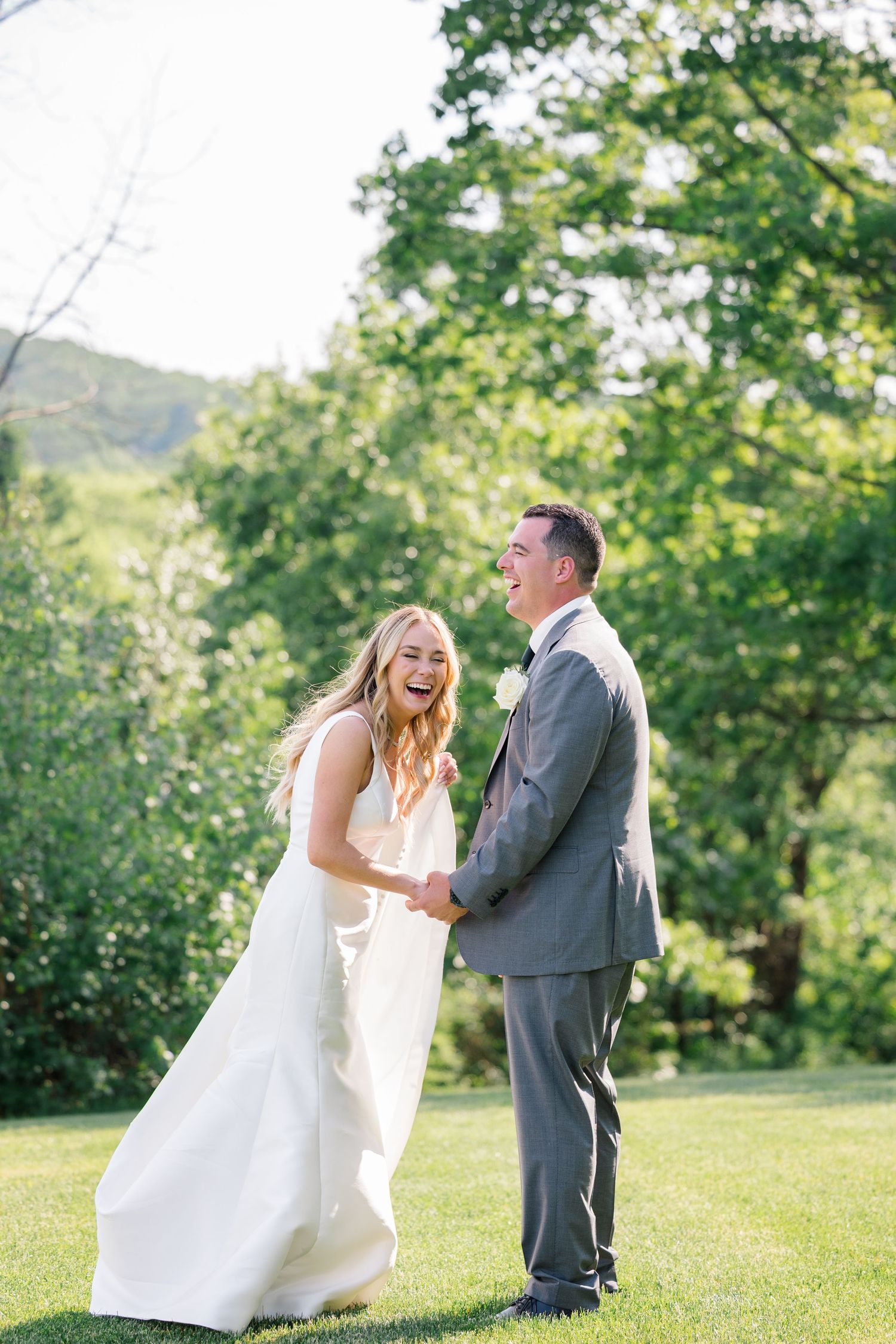 Joyful wedding moment captured outdoors against a lush green hillside background.