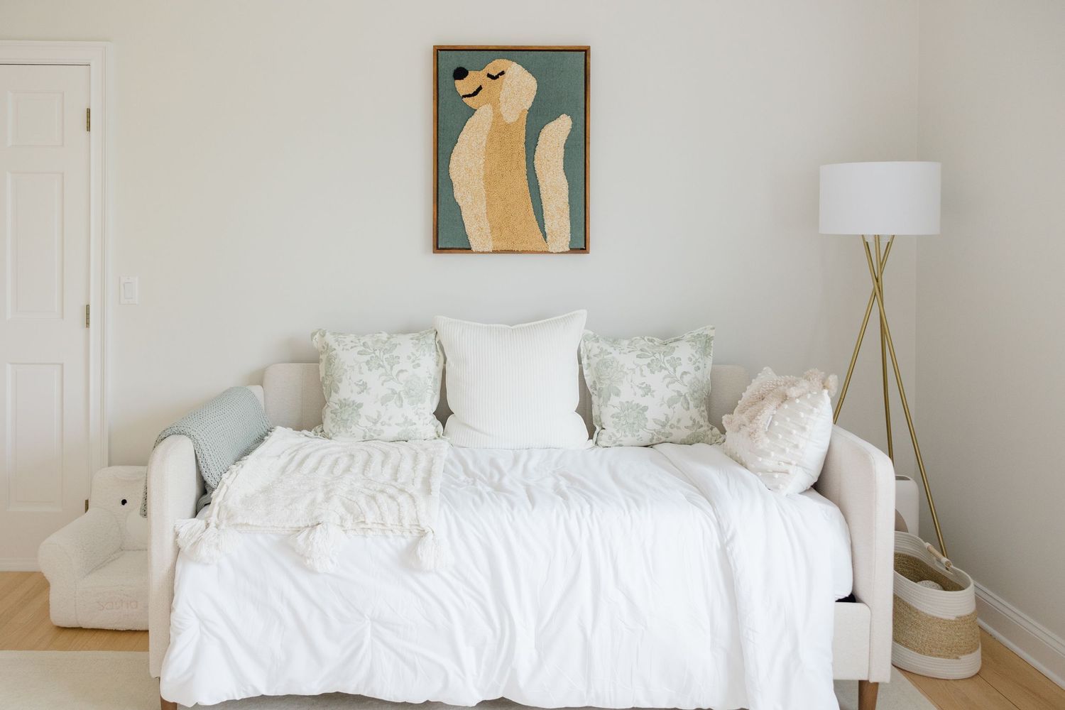 A modern minimalist bedroom with a white bed and neutral walls featuring simple geometric wall art and wooden accents.