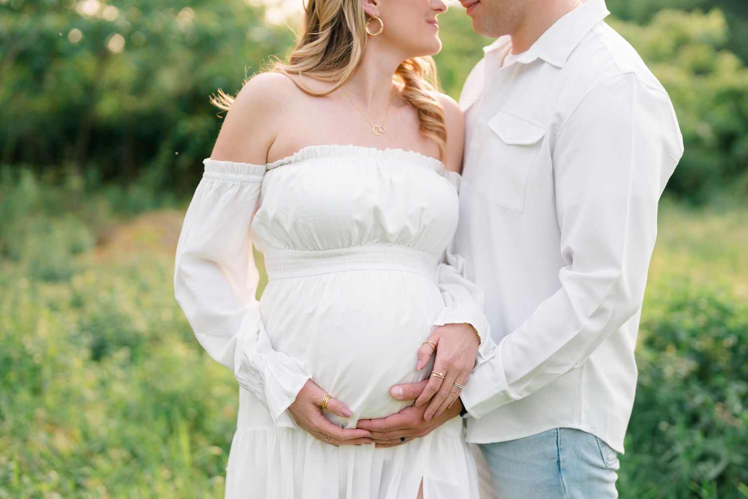 Sweet maternity photography with couple wearing white and embracing in nature setting.