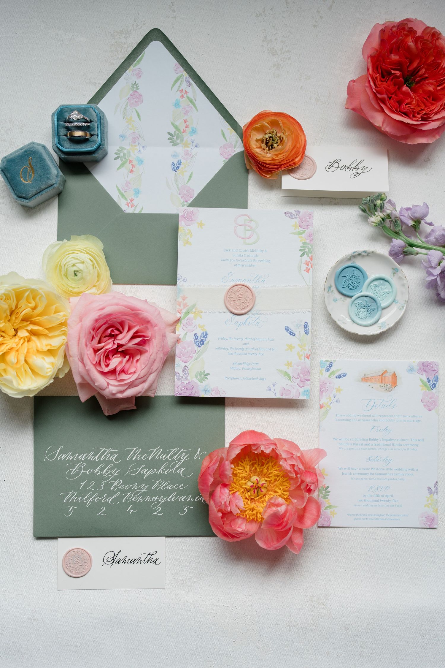 Elegant wedding invitation suite with florals, calligraphy and pastel details arranged on white surface.