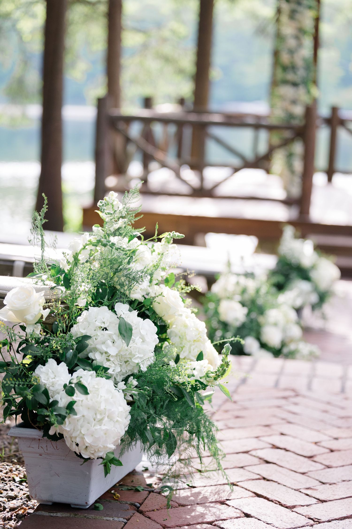 White hydrangea and greenery floral arrangement on a brick patio with a lake view.