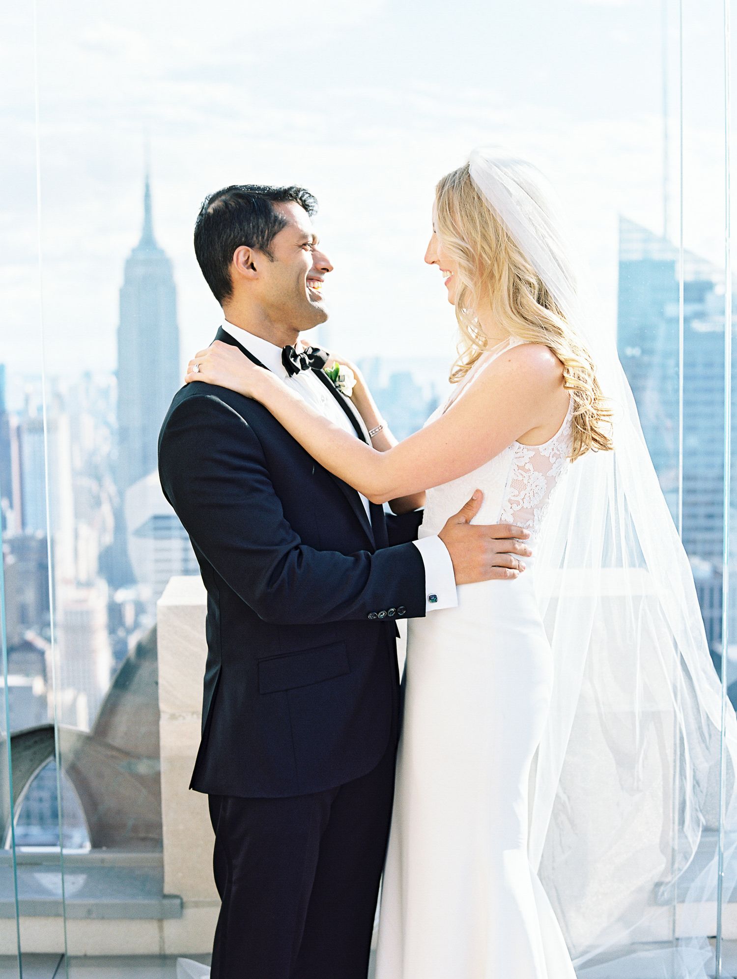 Newlyweds embrace joyfully with NYC skyline and Empire State Building in background.