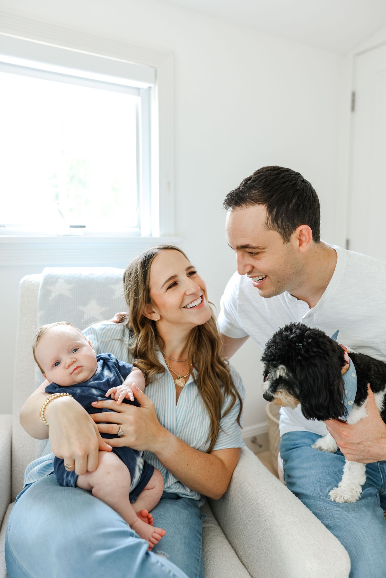 A cheerful family moment on a white couch with their black and white dog in a bright modern living room.