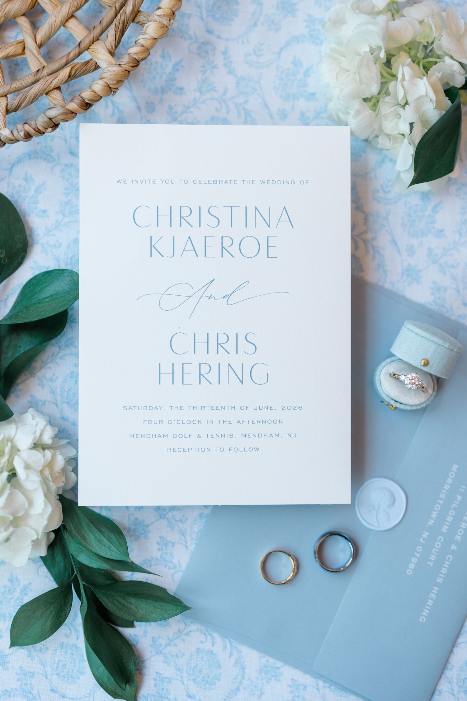 Elegant blue and white wedding invitation for Christina Kjaeroe and Chris Hering with rings and floral accents.