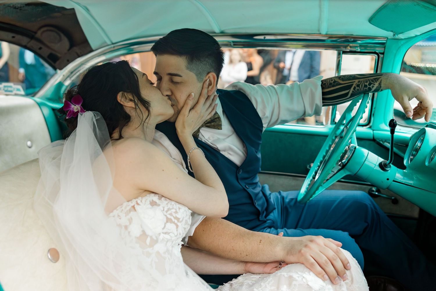 A couple kisses in the turquoise interior of a classic vintage car on their wedding day.