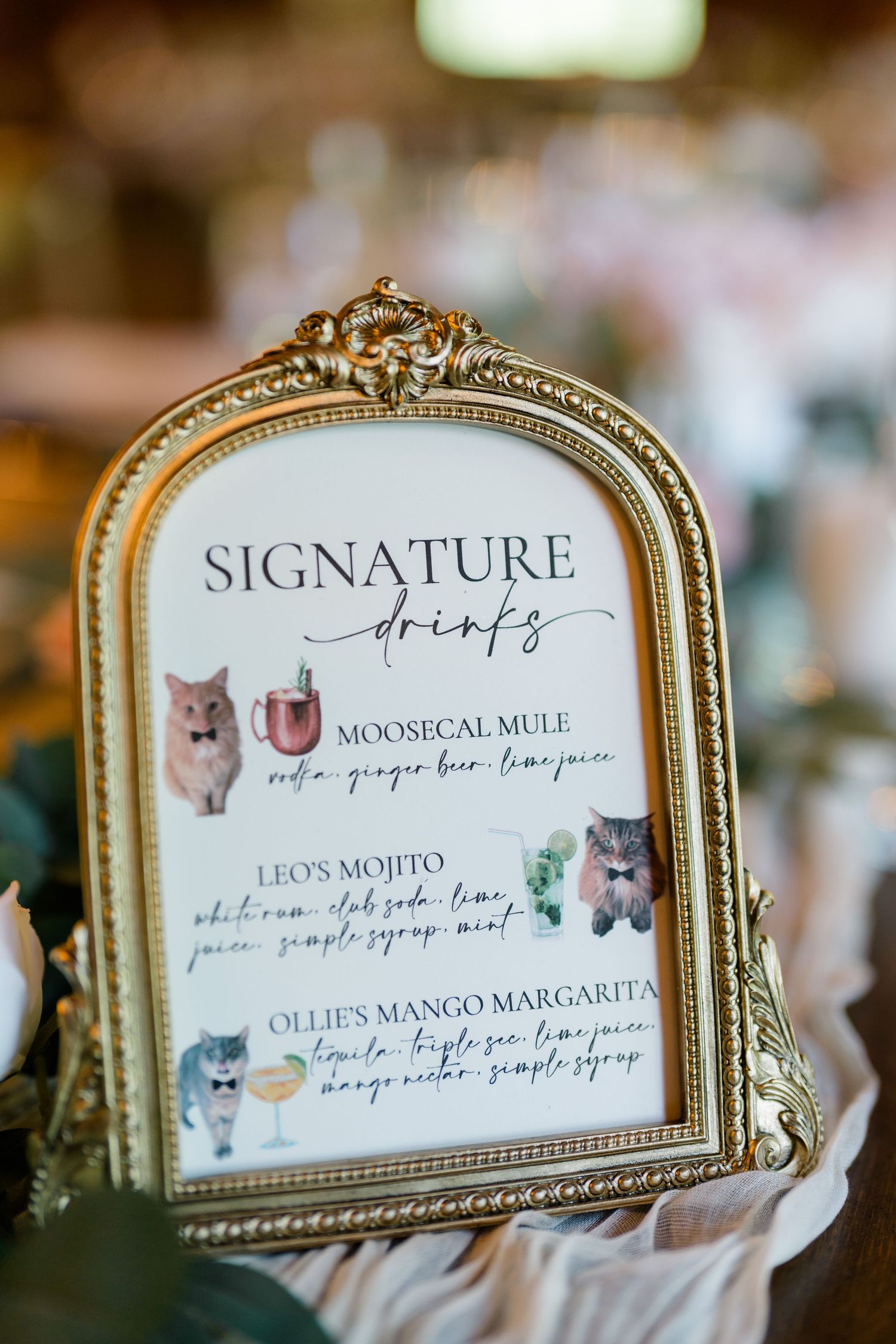 Vintage gold-framed signature drinks menu featuring cocktails with hamster illustrations at a wedding reception.