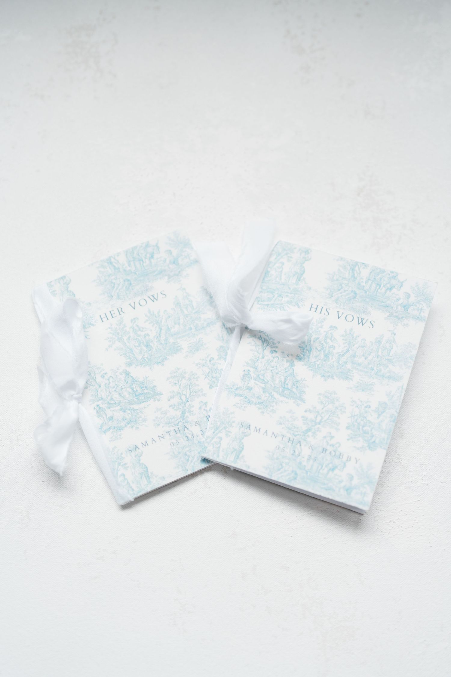 Two light blue and white patterned wedding vow books with delicate floral designs on a white background.