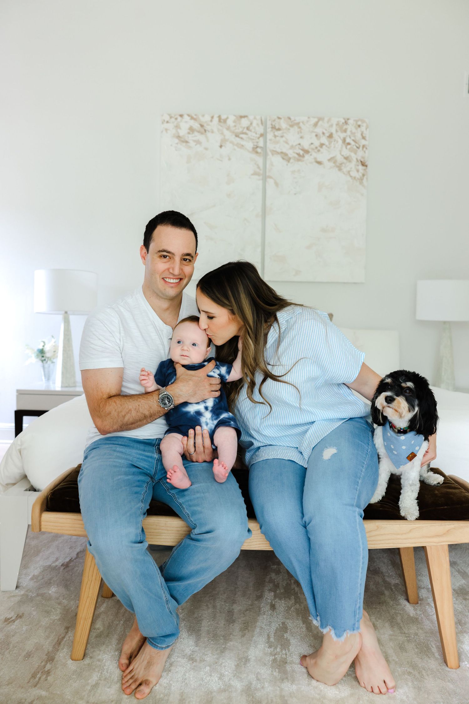 A family sits on a wooden bench in a bright room with their small black and white dog.