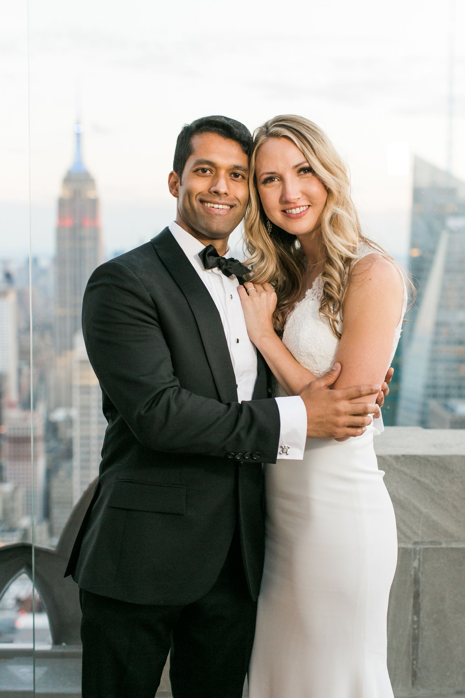 A wedding couple poses on a rooftop with the Empire State Building and NYC skyline in the background.