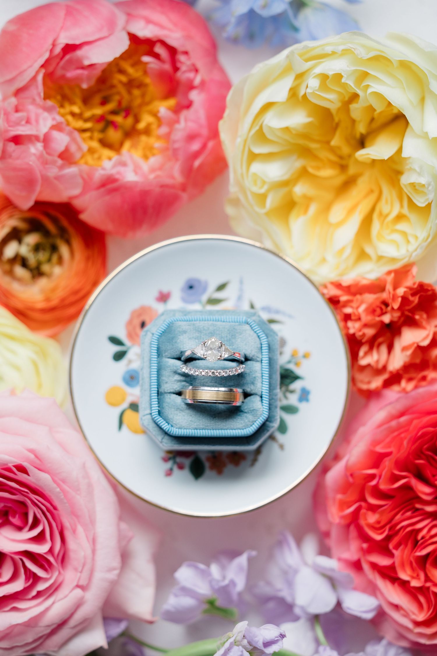 Wedding rings displayed on delicate blue plates surrounded by pink and white roses.