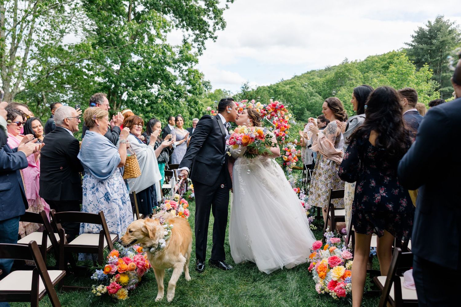Wedding guests enjoying an outdoor reception under trees with colorful floral decorations.
