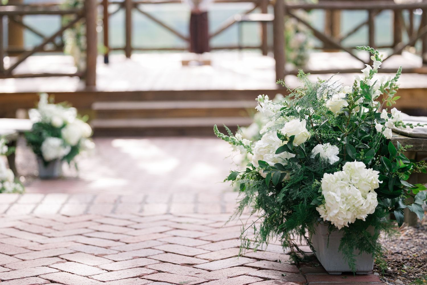 White hydrangea flowers and greenery in decorative pots on a herringbone brick patio with railing in background.