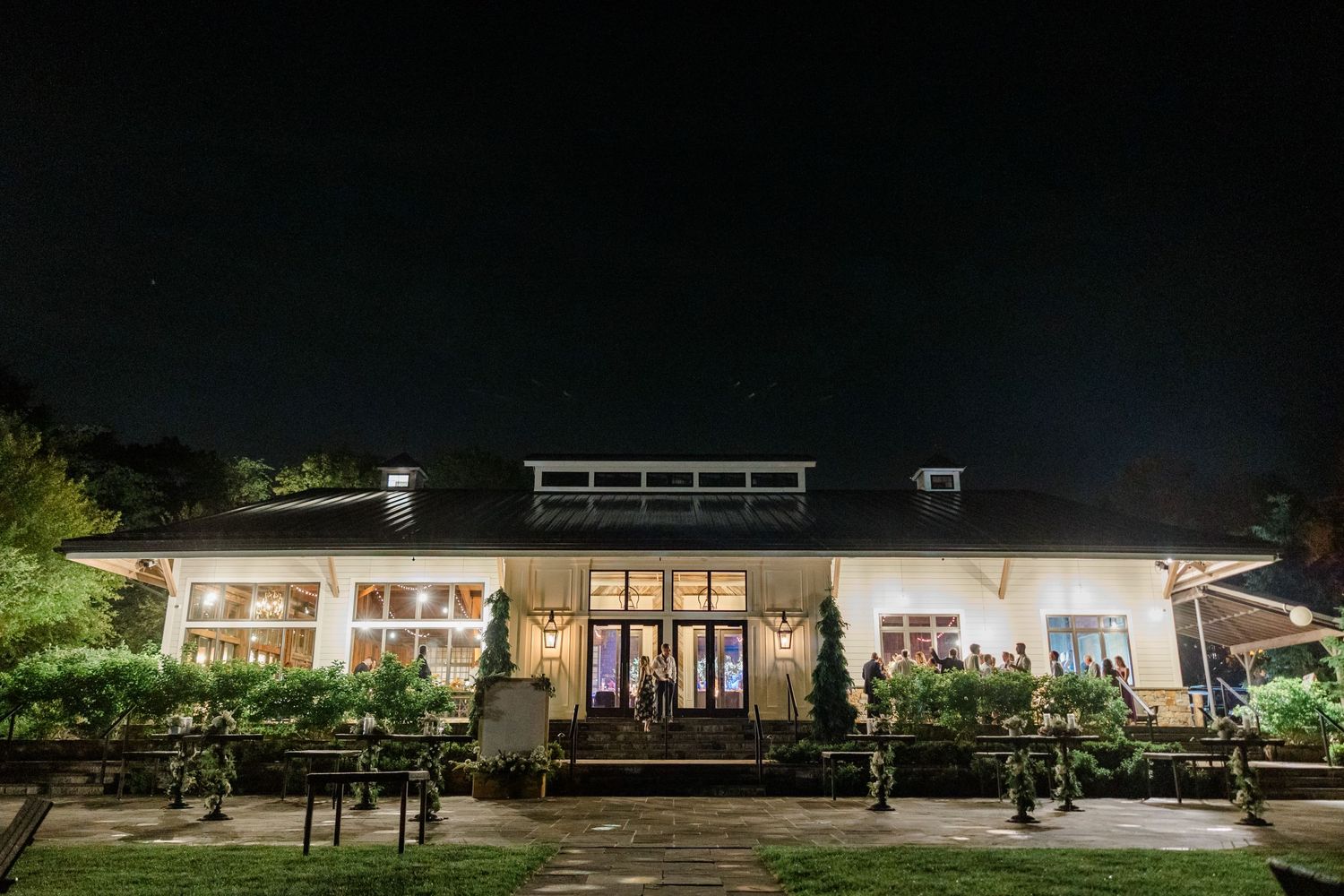 Illuminated white wedding venue exterior at night with manicured landscaping.