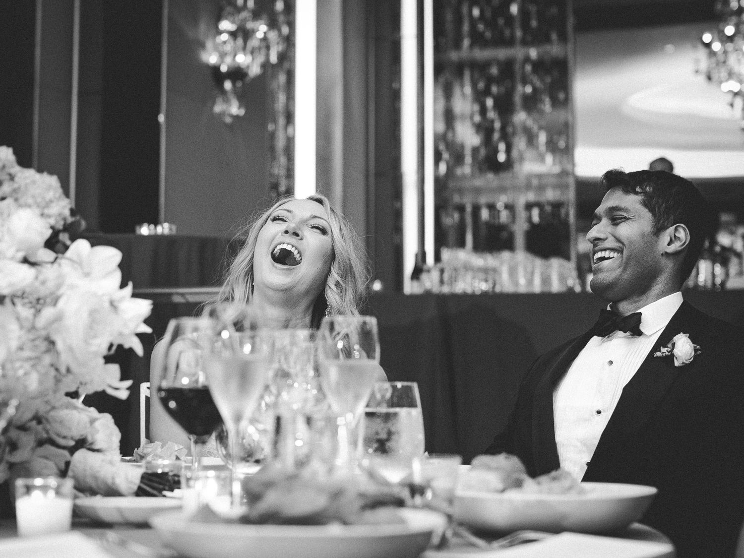 A heartwarming black and white photo capturing genuine laughter shared during a wedding reception dinner.