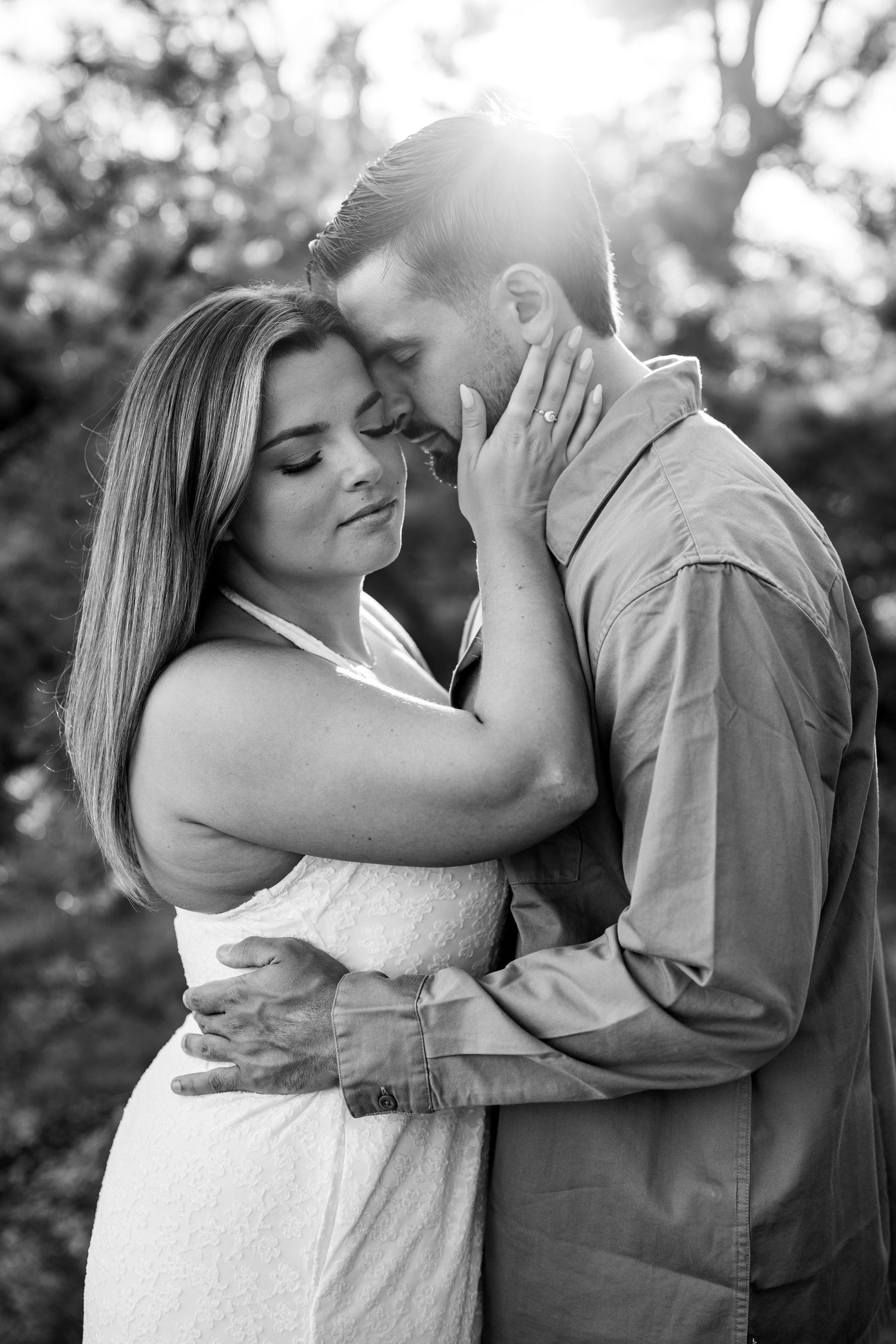 Black and white photo of a romantic couple embracing outdoors, woman in white dress tenderly touching mans face.