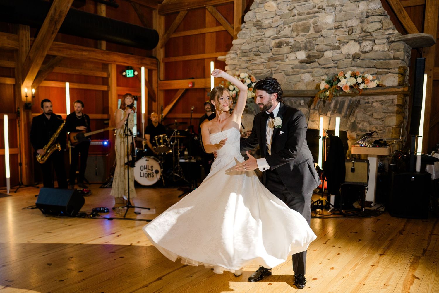 Bride and groom share first dance in rustic barn venue with live band performing in background.