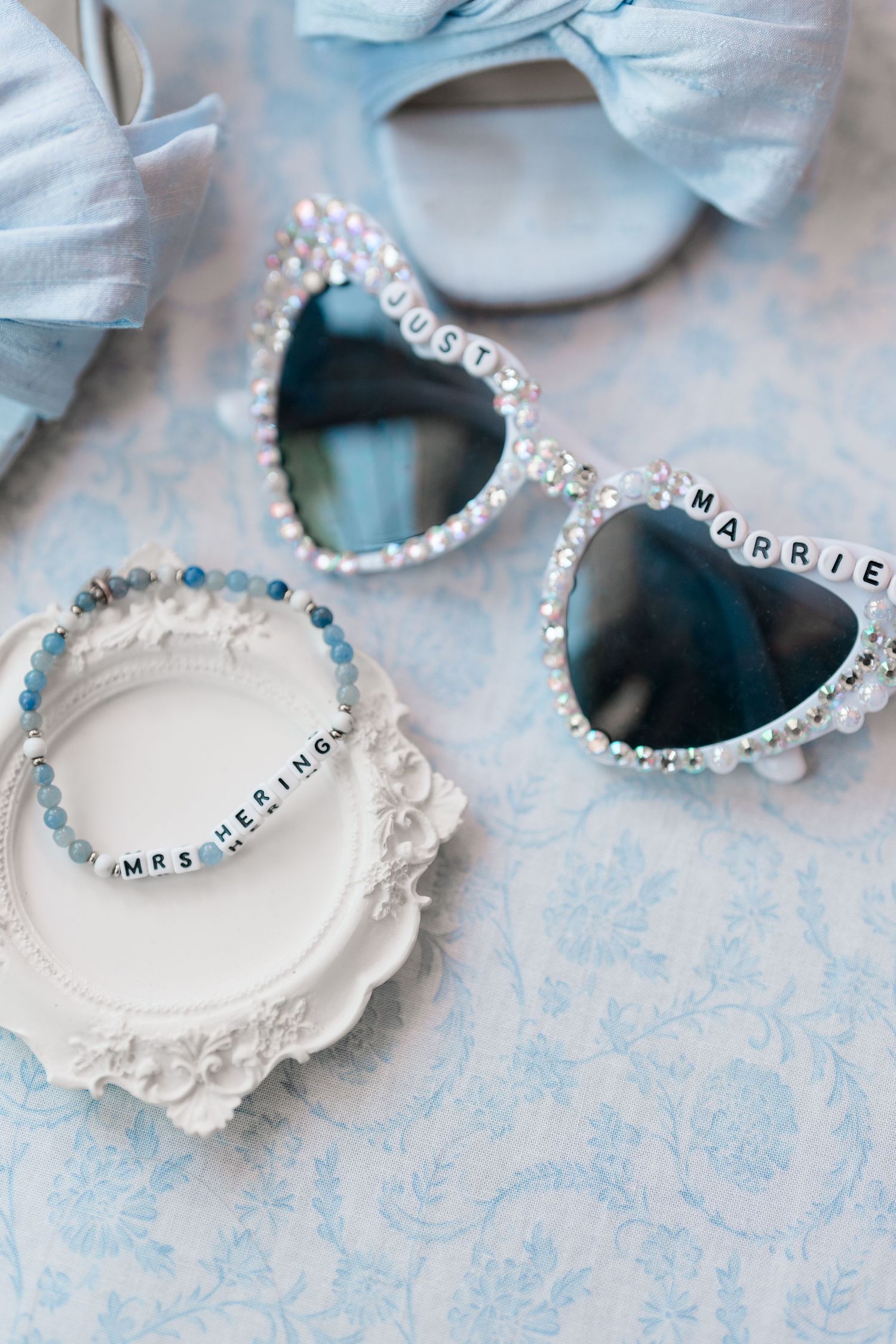 Pearl-adorned heart sunglasses reading Just Married with a beaded Mrs bracelet on a white decorative tray.