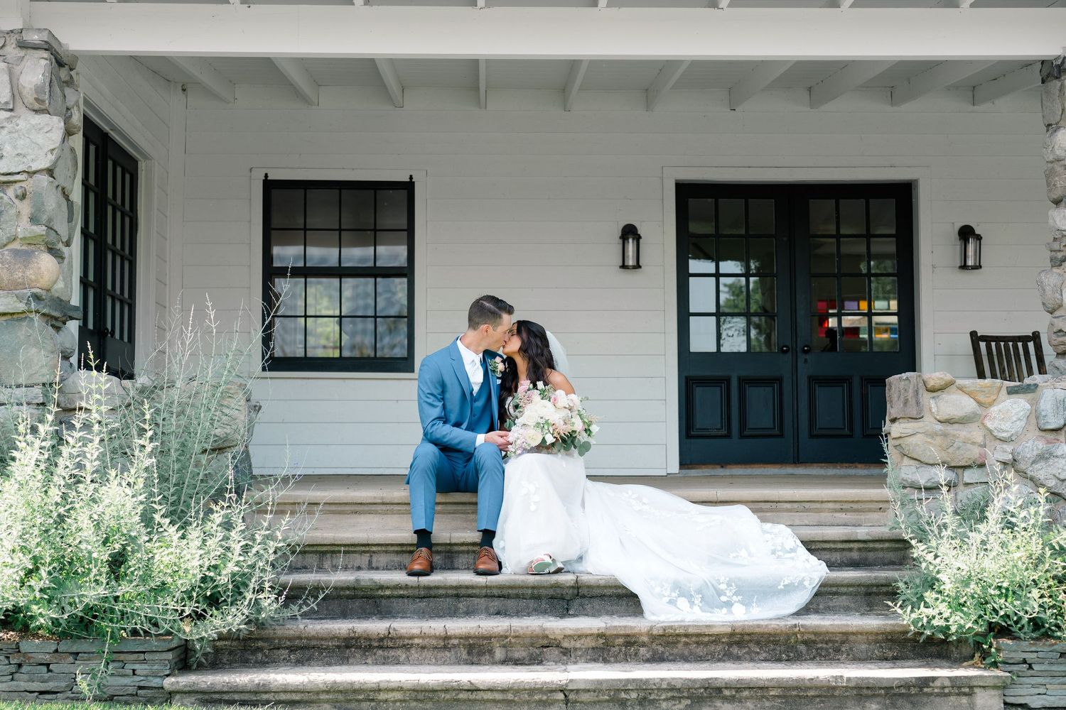 Intimate wedding moment captured on white porch steps with rustic stone details.