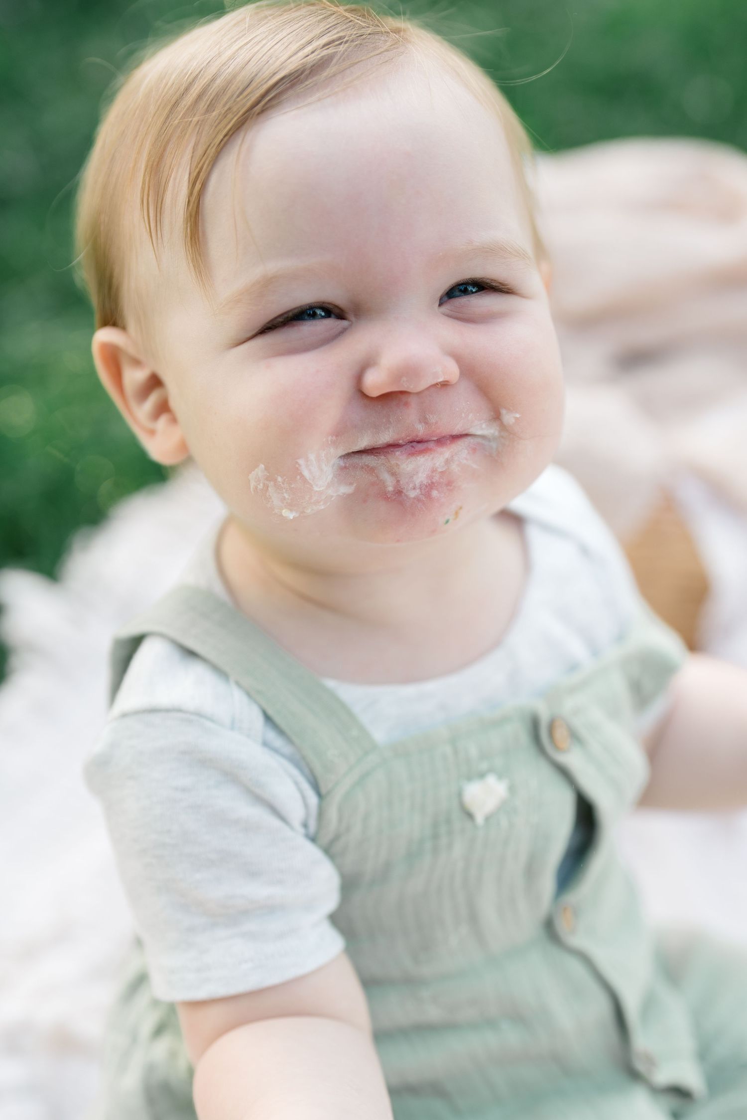 Happy baby boy smiling with white frosting on his face during first birthday cake smash.
