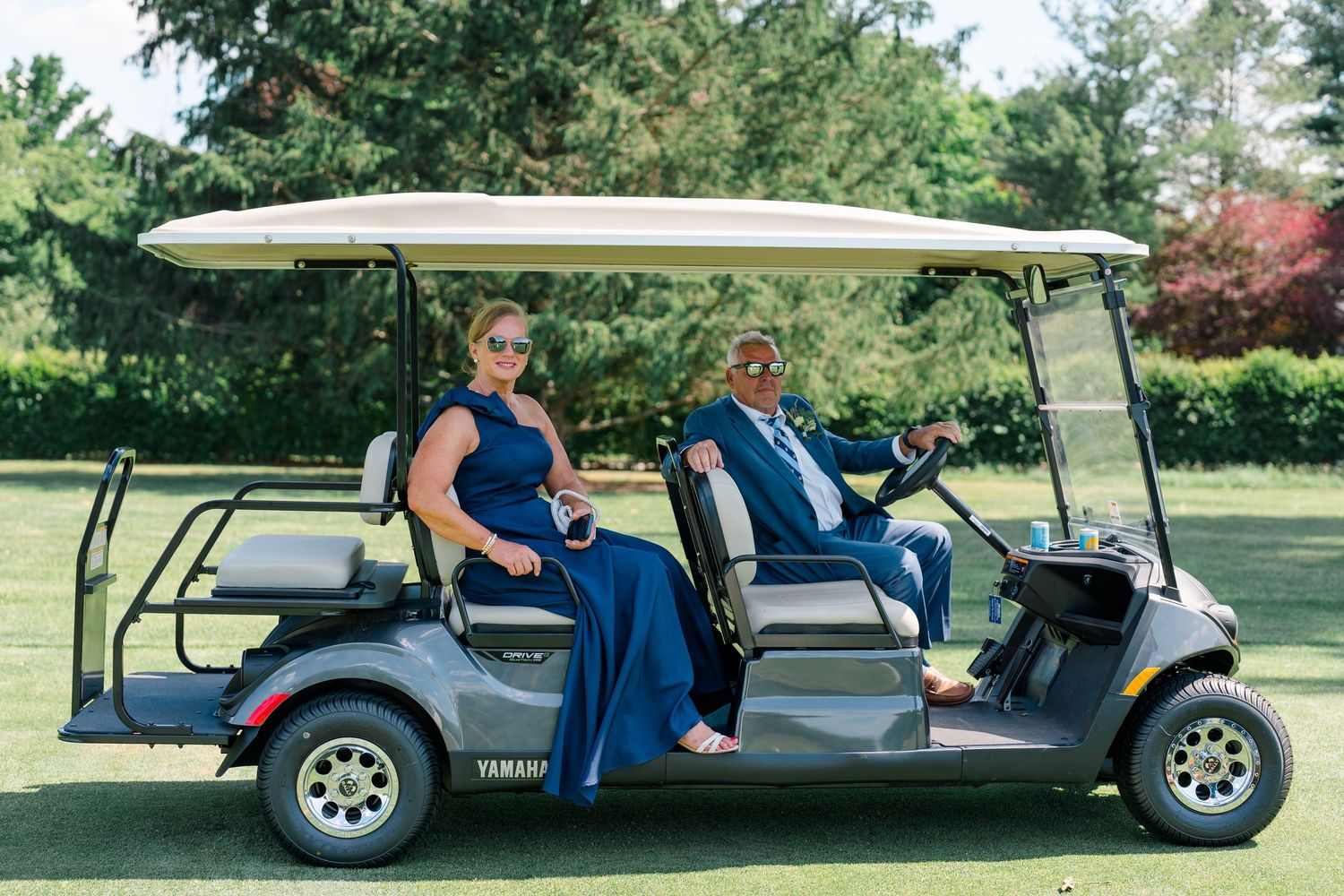 Couple in formal attire riding a Yamaha golf cart on a lush green golf course.