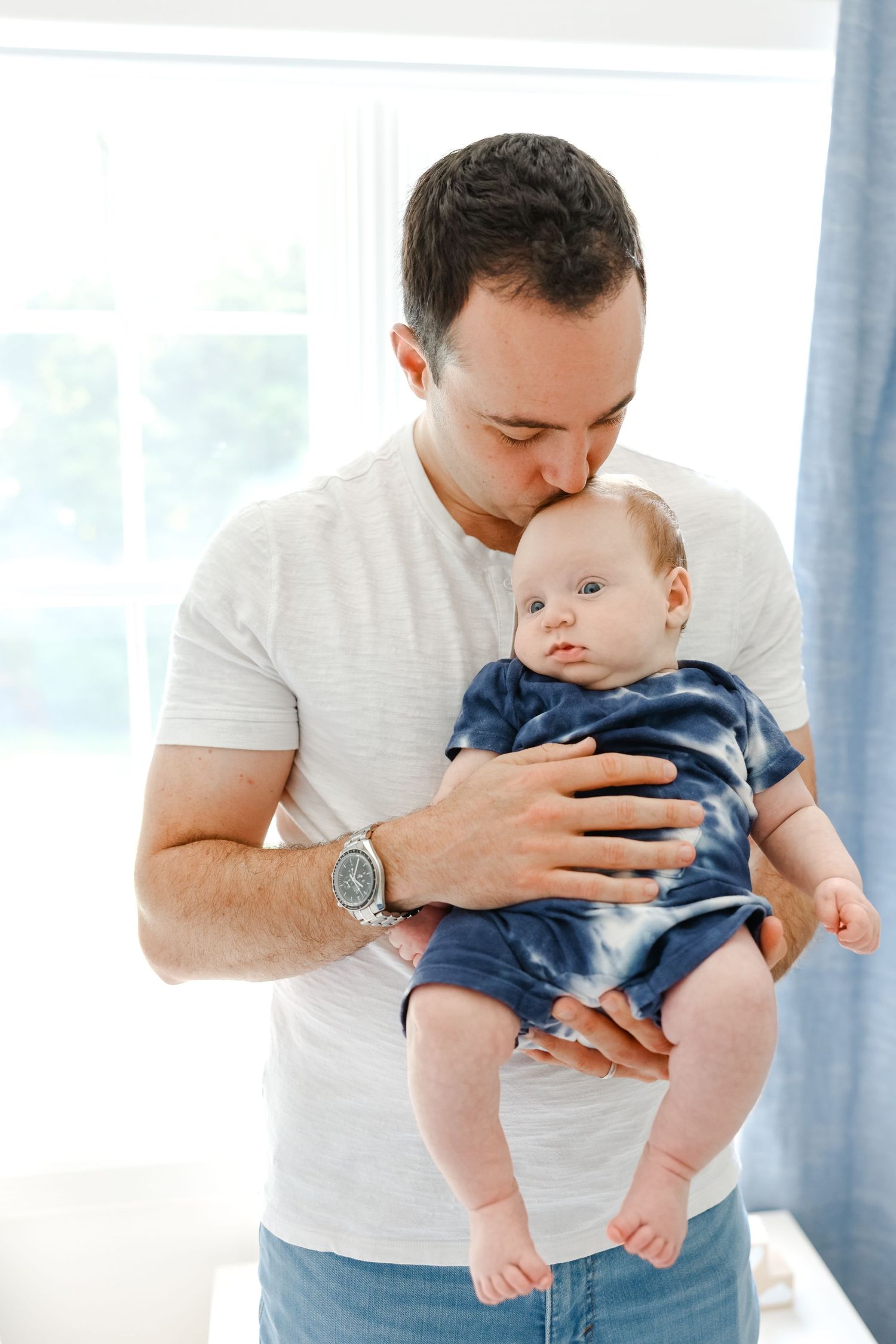 A tender parenting moment captured in a bright indoor setting with natural window light.