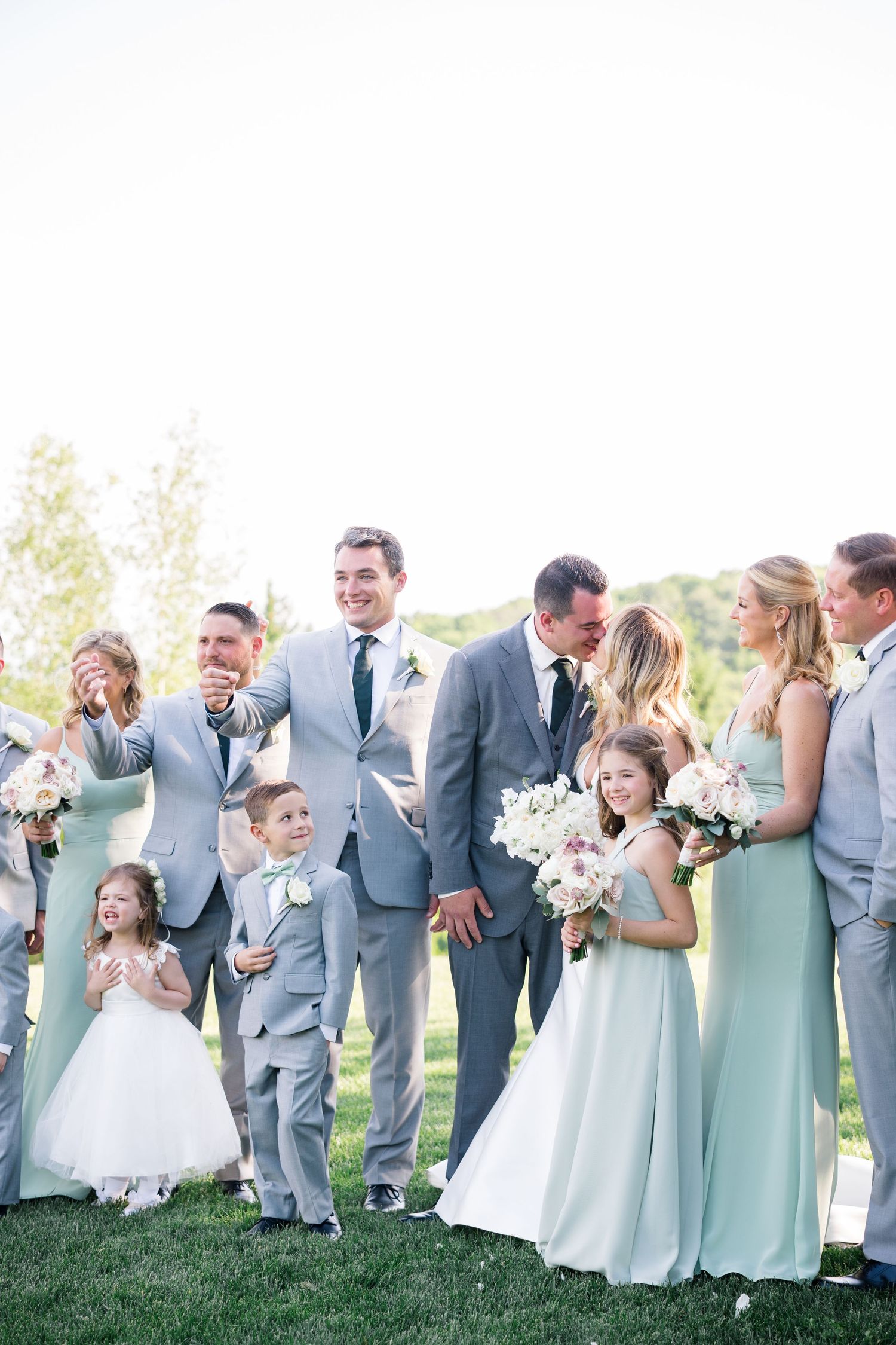Wedding party in mint green dresses and gray suits posing together on a sunny lawn.