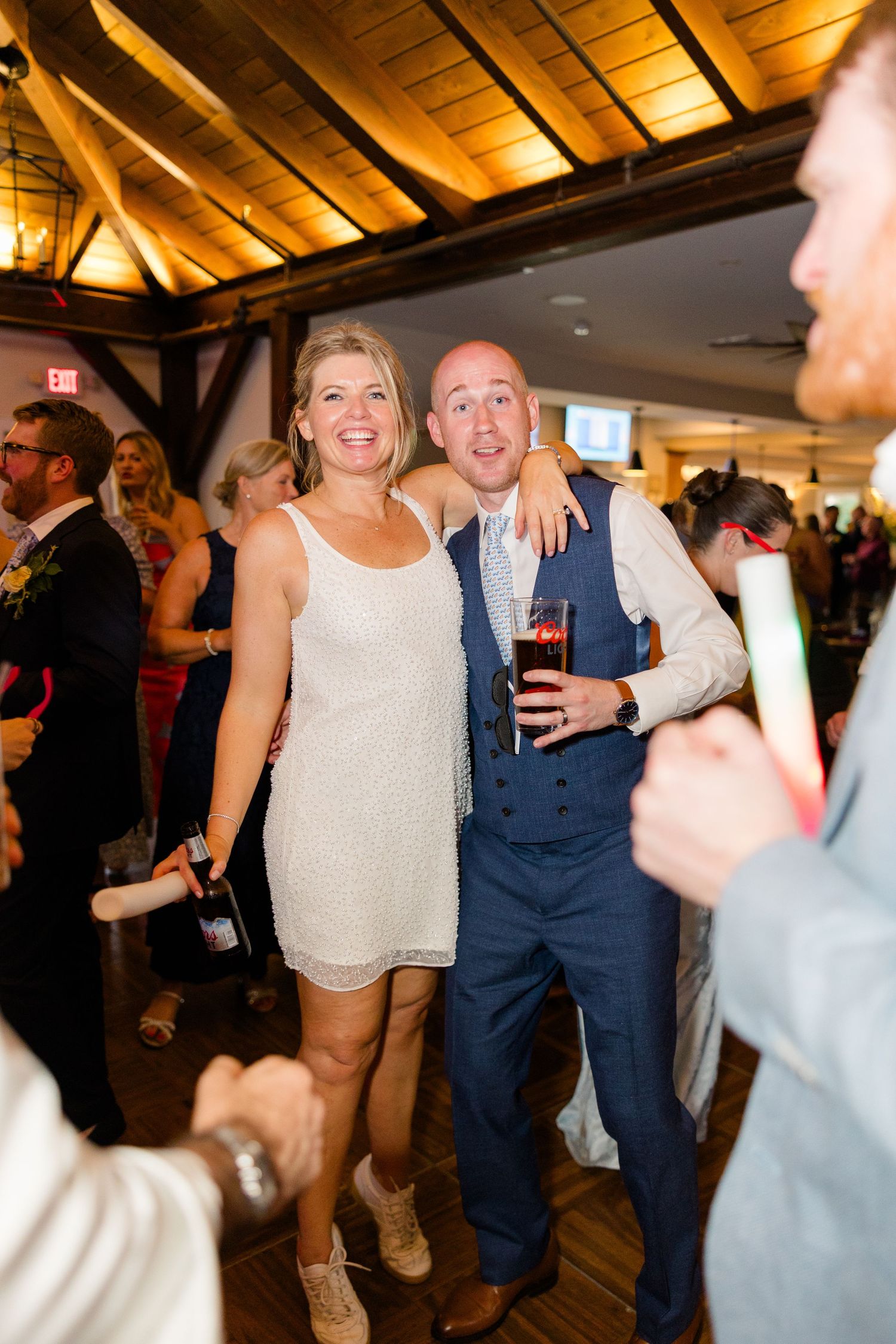 Bride in short sequin dress and groom in navy suit smile together on the dance floor at wedding reception.