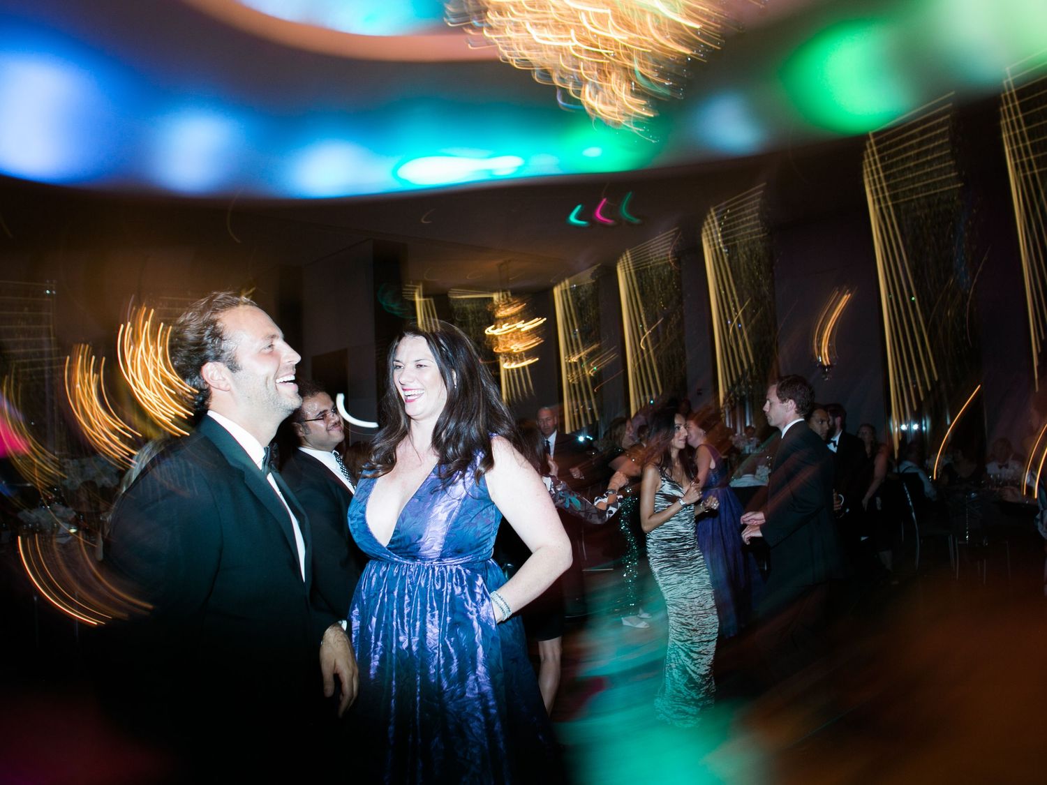 People dancing at a festive event with blurred colorful lights and motion effects in the background.