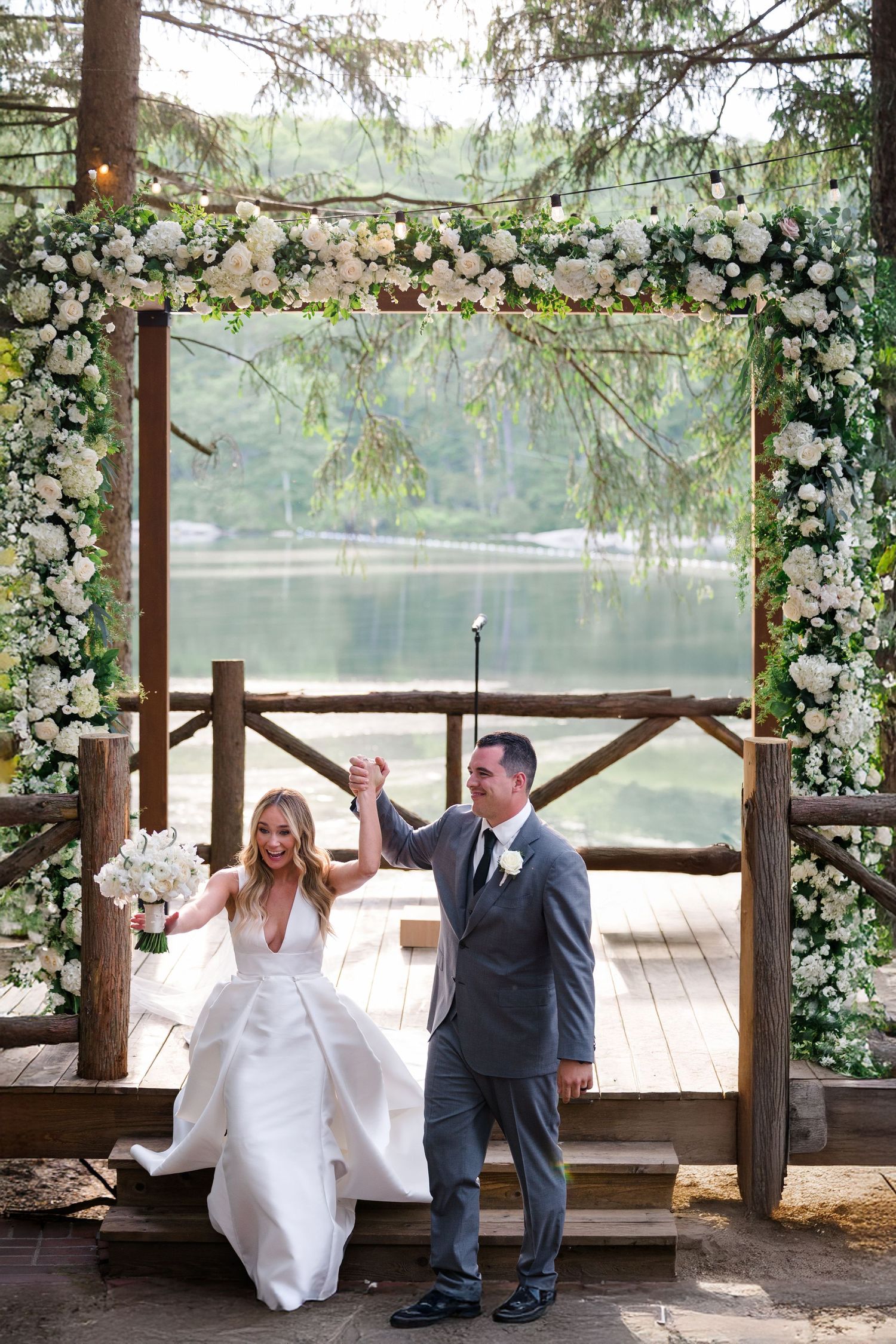 A romantic wedding ceremony under a floral arch overlooking a serene lake.