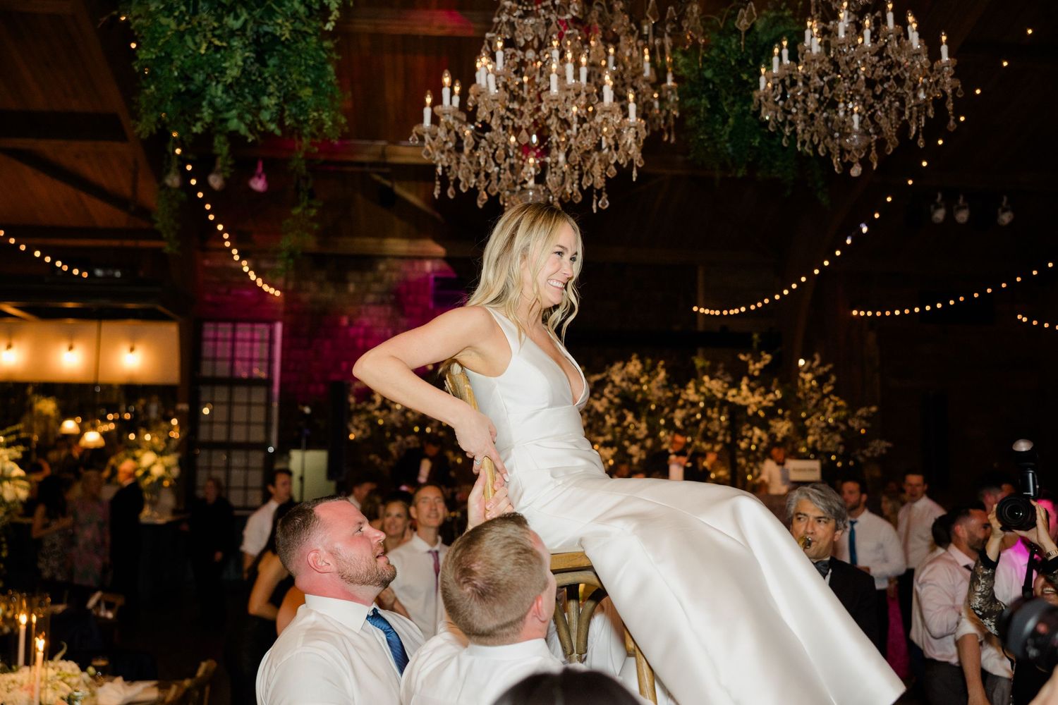 Wedding celebration with couple participating in traditional chair lifting dance.